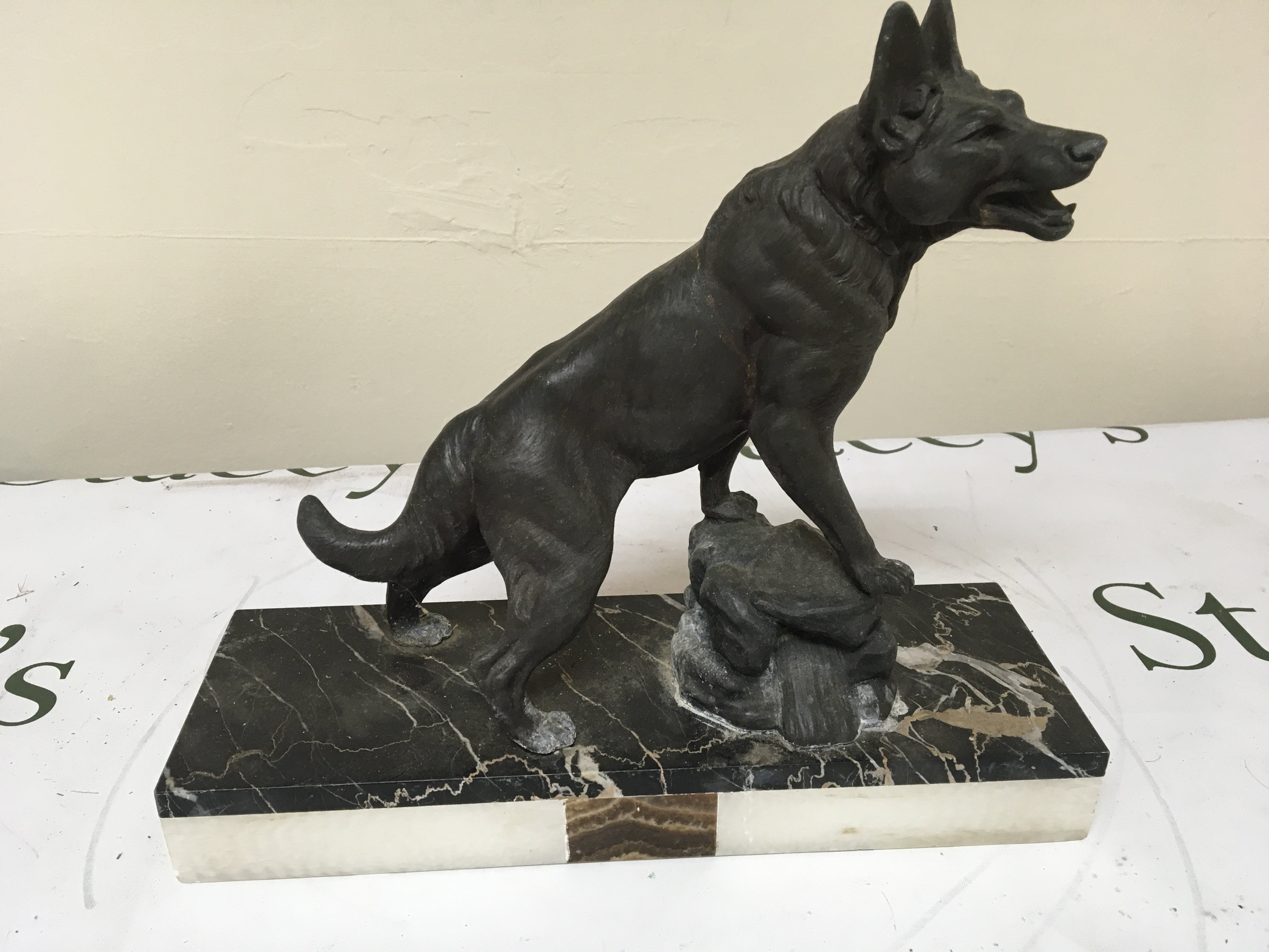 An Art Deco figure of a dog resting on a rock with a multi coloured rectangular marble base. 30cm wide