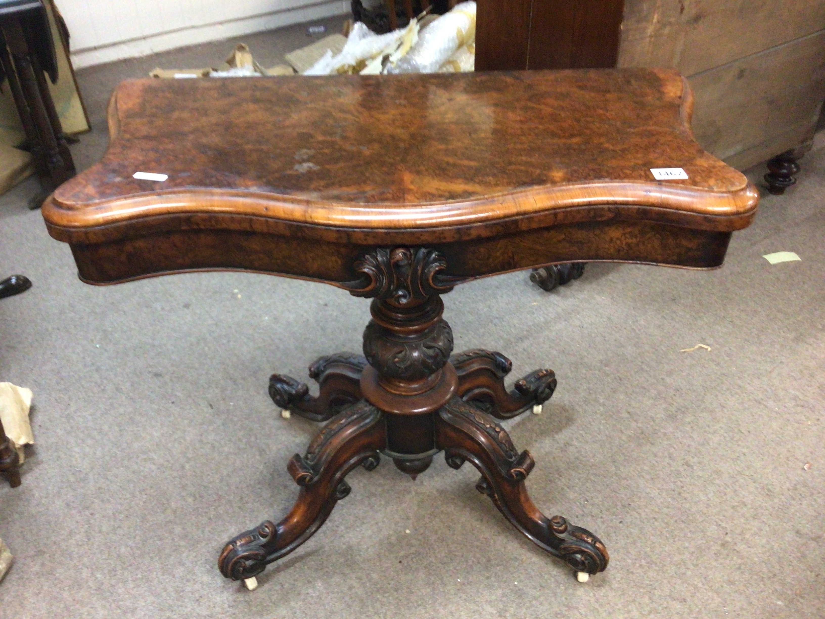 A Victorian burr walnut serpentine card table the hinged top on a turned column on carved cabriole legs.