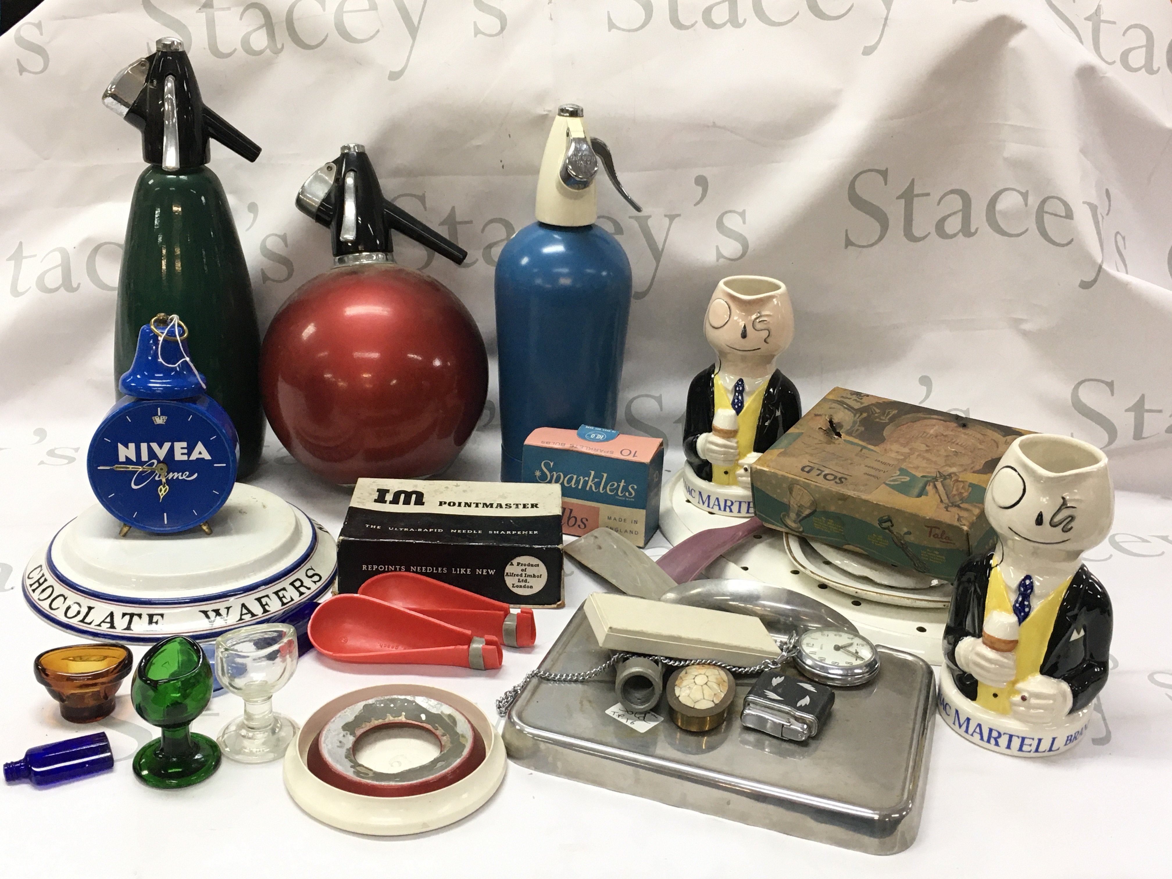 Vintage items including Cognac Martell Brandy jug figures, soda streamers , Nivea alarm clock, porcelain chocolate wafers stand , chrome Rozalex cream dispenser , brass aeroplane , glass eye baths etc . This lot cannot be posted