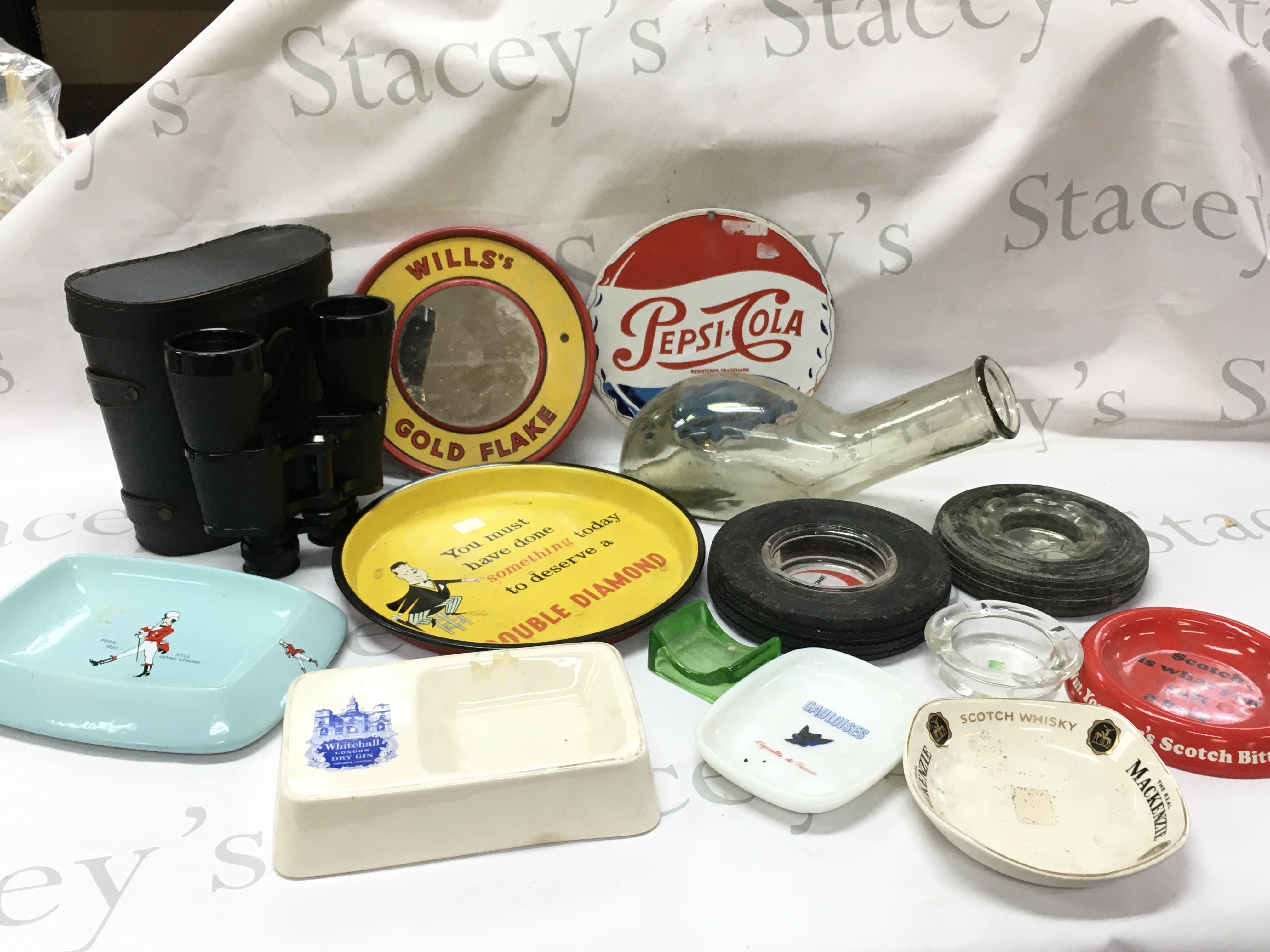 Vintage items including a ceramic Wade Johnnie Walker ashtray, Mackenzie scotch whiskey ashtray, double diamond tray, wills gold flake cigarettes mirror, Pepsi cola sign , tyre ash trays, Cheiza Zenith 12x50 binoculars ,glass urinal bottle. This lot cannot be posted