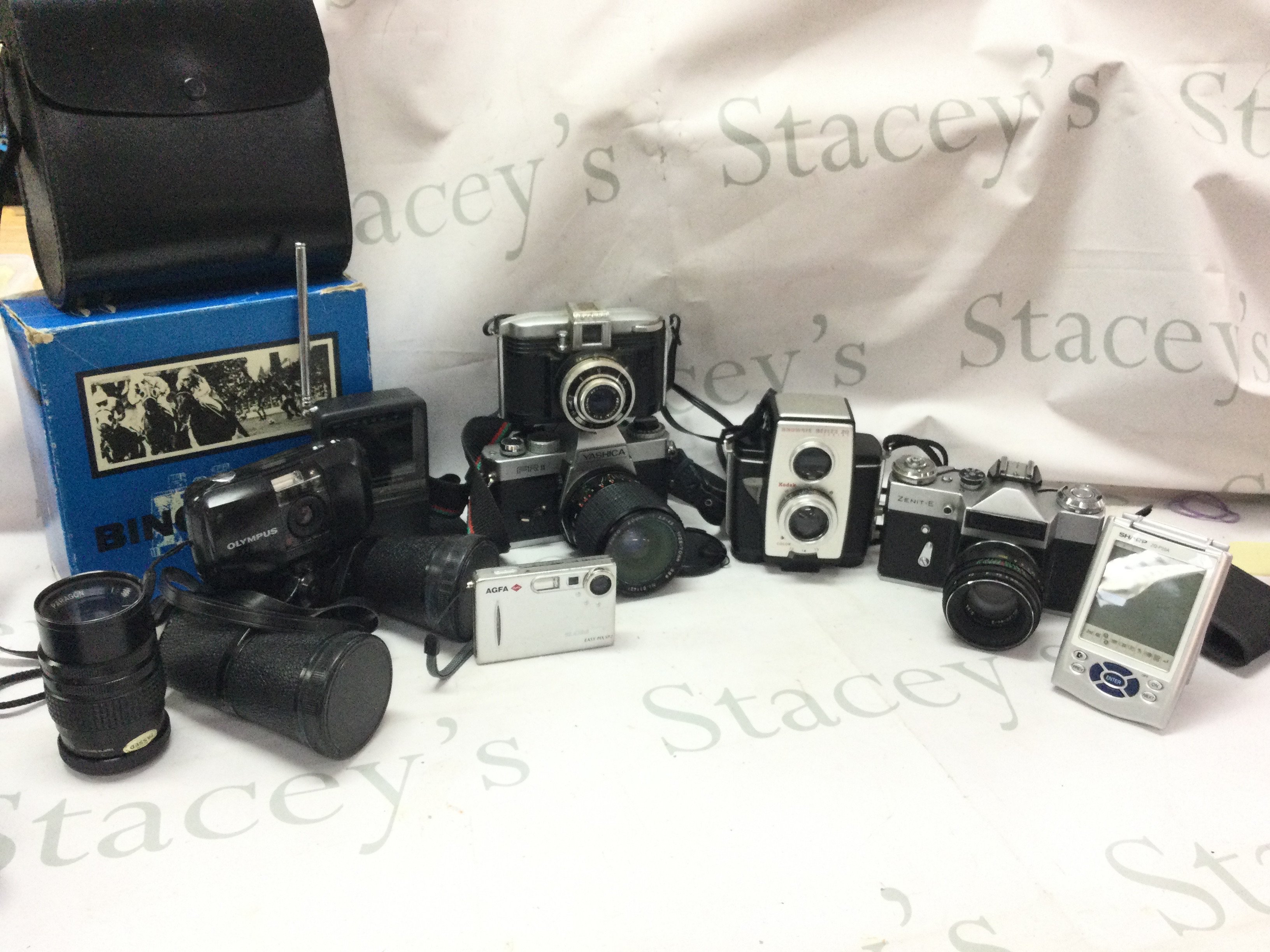A collection of cameras including Brownie Reflex 20, Zenit-E, Yashica Fr II, Olympus , Mark Scheffel 10x50 binoculars, Casio EV-500, Ferrania. Postage category C