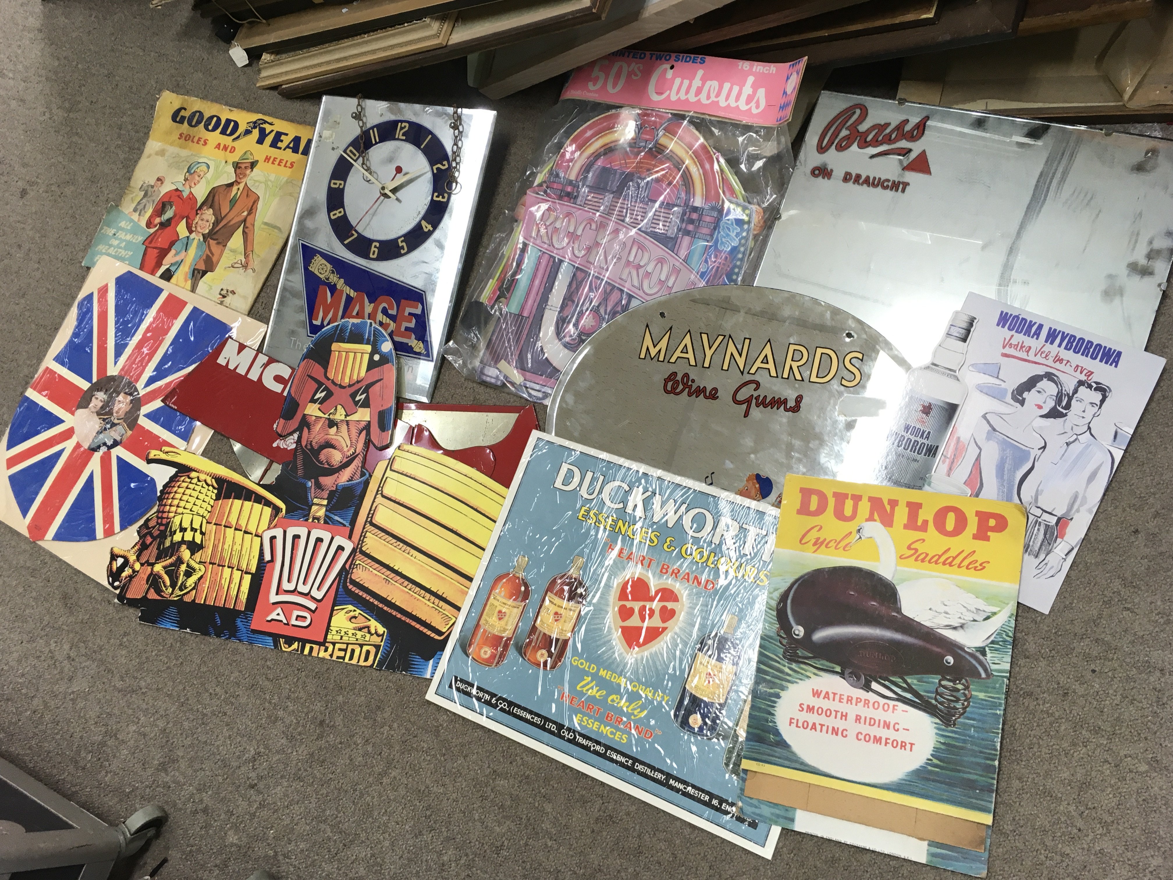 A collection of advertisements including Bass on draught and Maynard wine gum mirrors, 2000AD judge dread cardboard advertisement, Duckworths sign, Dunlop cycle saddles cardboard standee, Mage mirror clock, Michelin tyre display stand . We cannot post this lot.