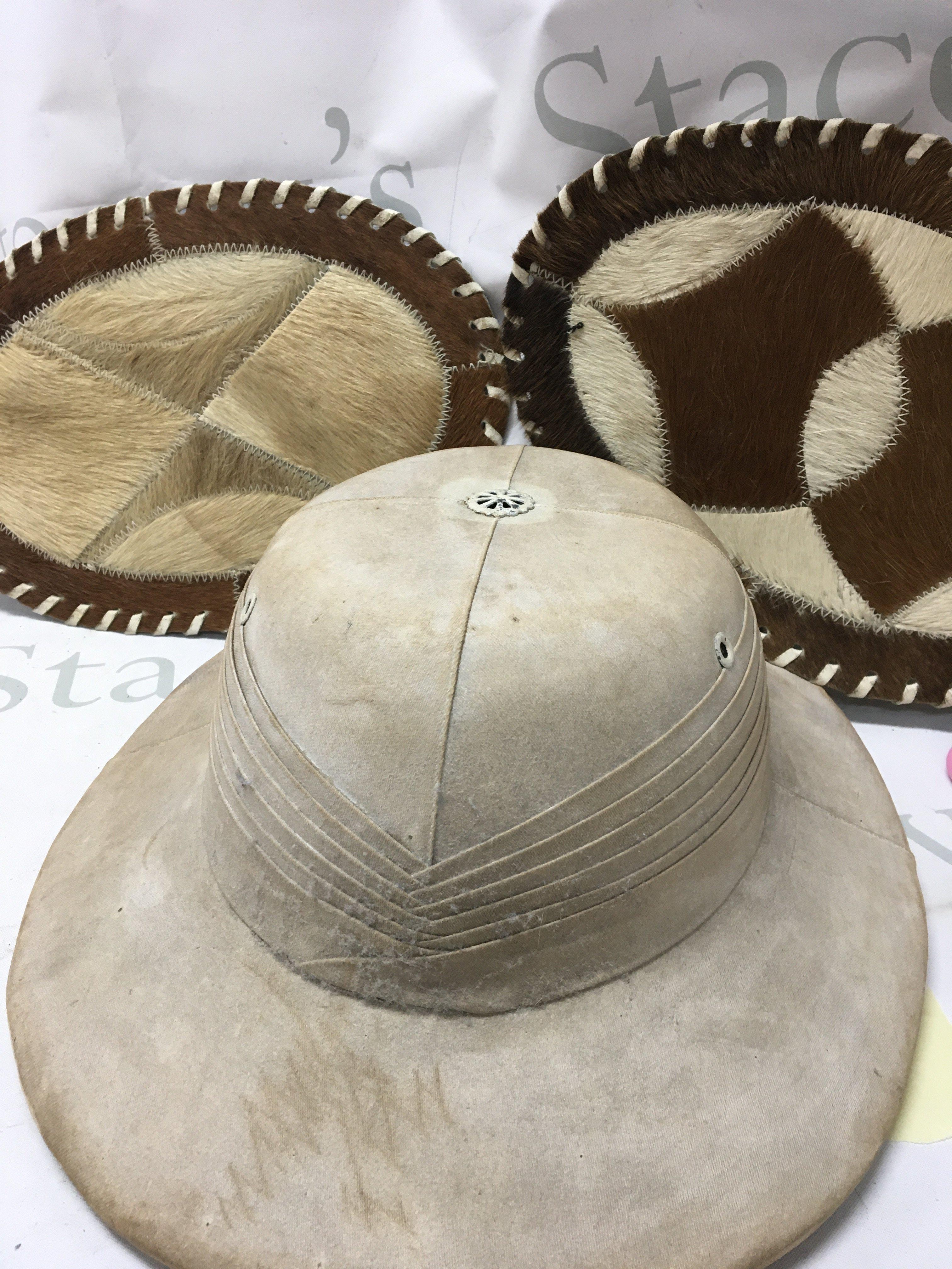 A pith helmet and two oval goat skin mats .