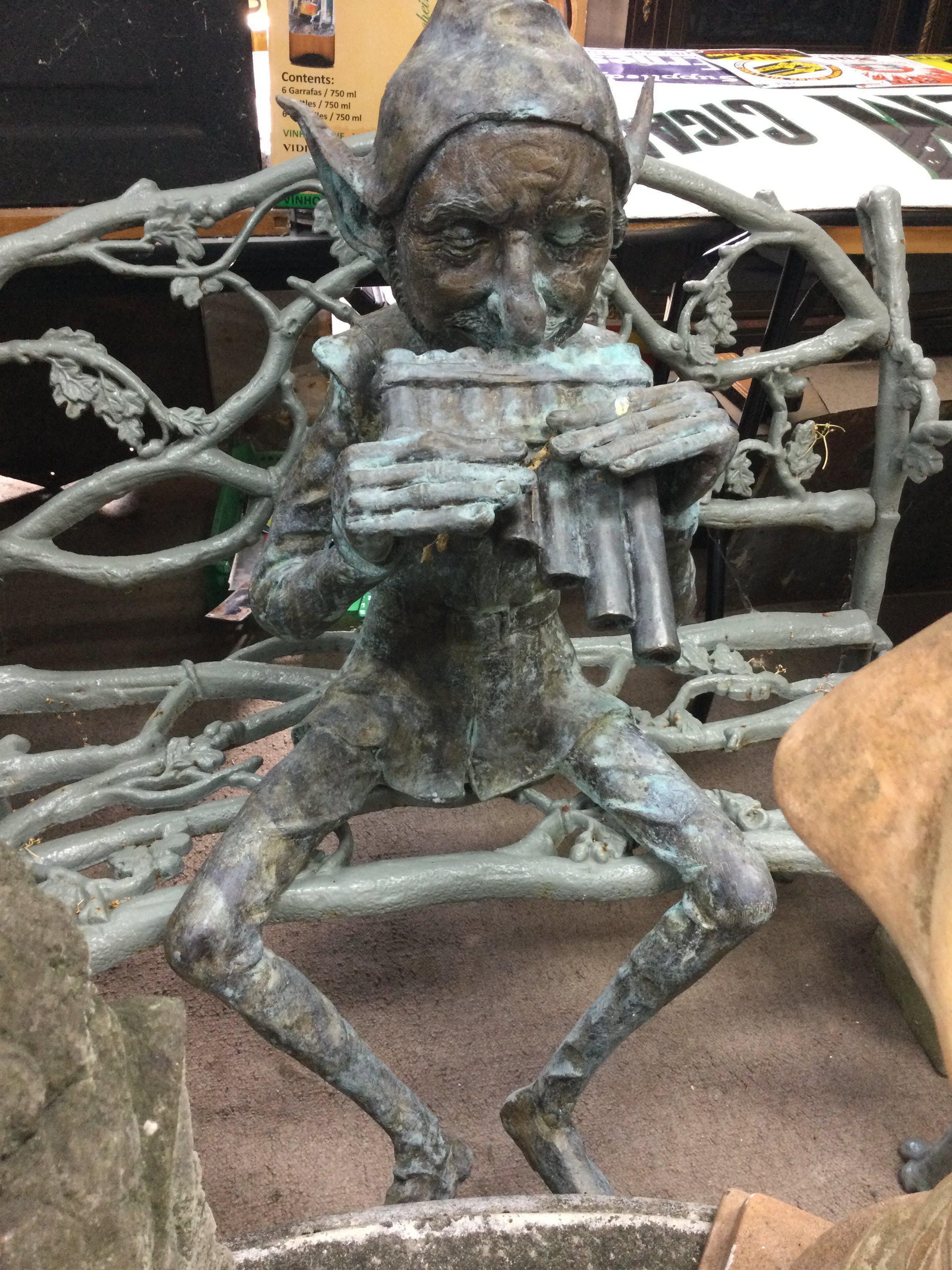 A bronze pixie figure seated playing pipes 120 cm .