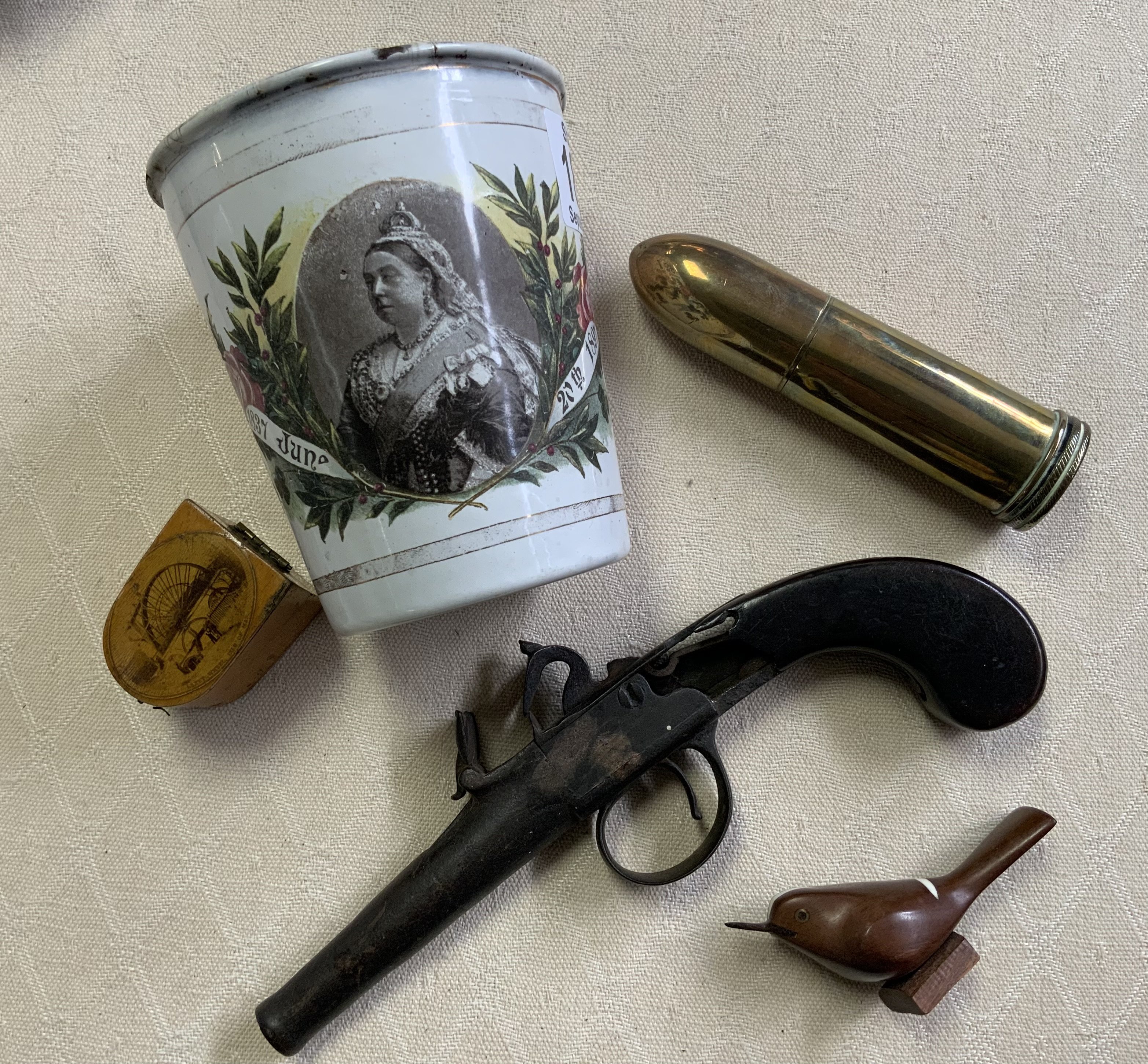 A Victorian enamel coronation beaker, Brass trench art lighter, Mauchline ware thimble case, Salla carved bird figure, early flintlock pistol in poor condition.