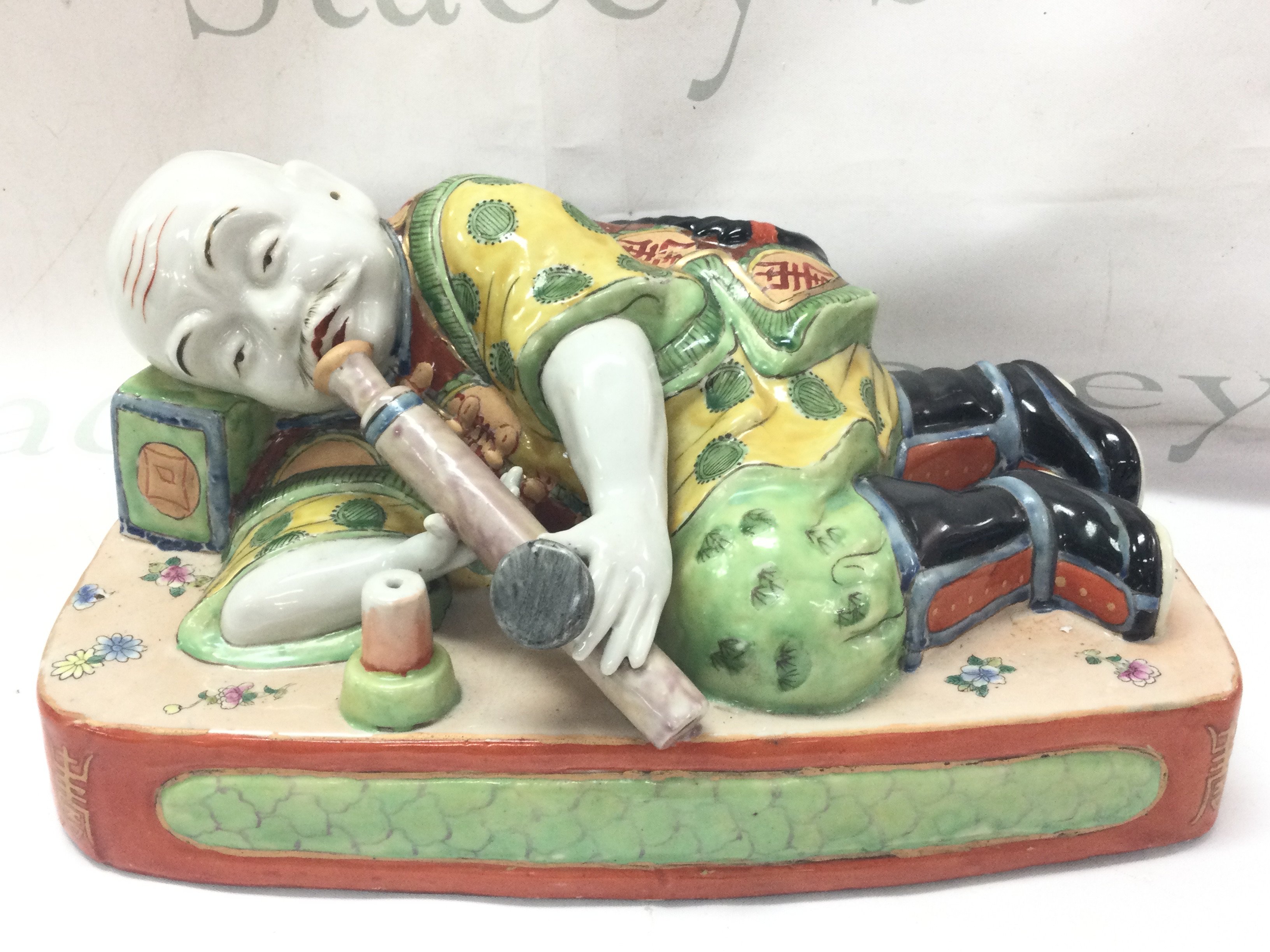 A 19th century Chinese porcelain figure of a sleeping opium smoker, with enamelled flower and Zhou motifs to garments. 15cm tall 32cm wide .this lot cannot be posted
