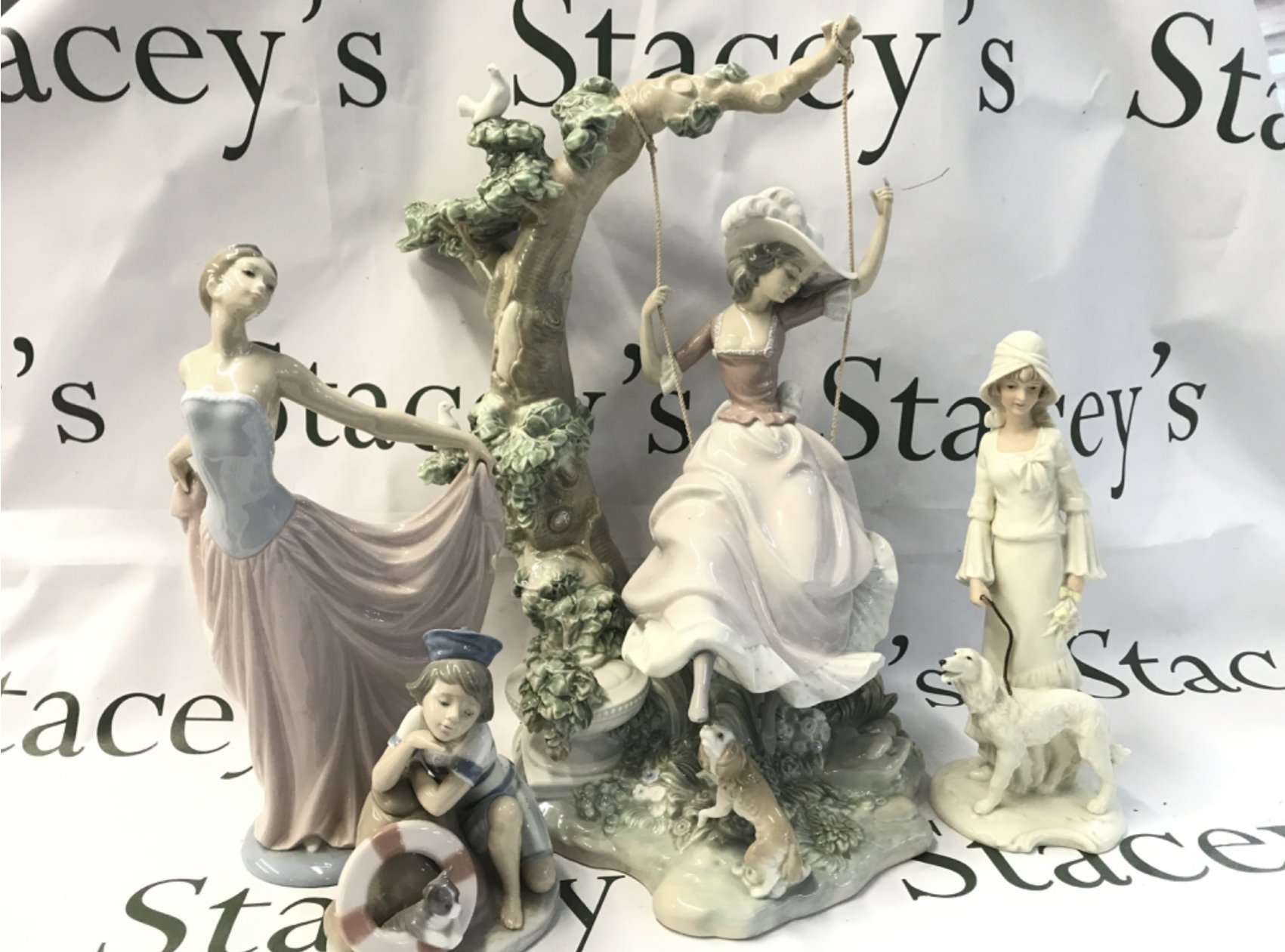 A large Lladro girl on swing figure (40cm tall), Lladro dancer figure, Mondays child sailor boy, SBL pride of place woman with dog figure. This lot cannot be posted