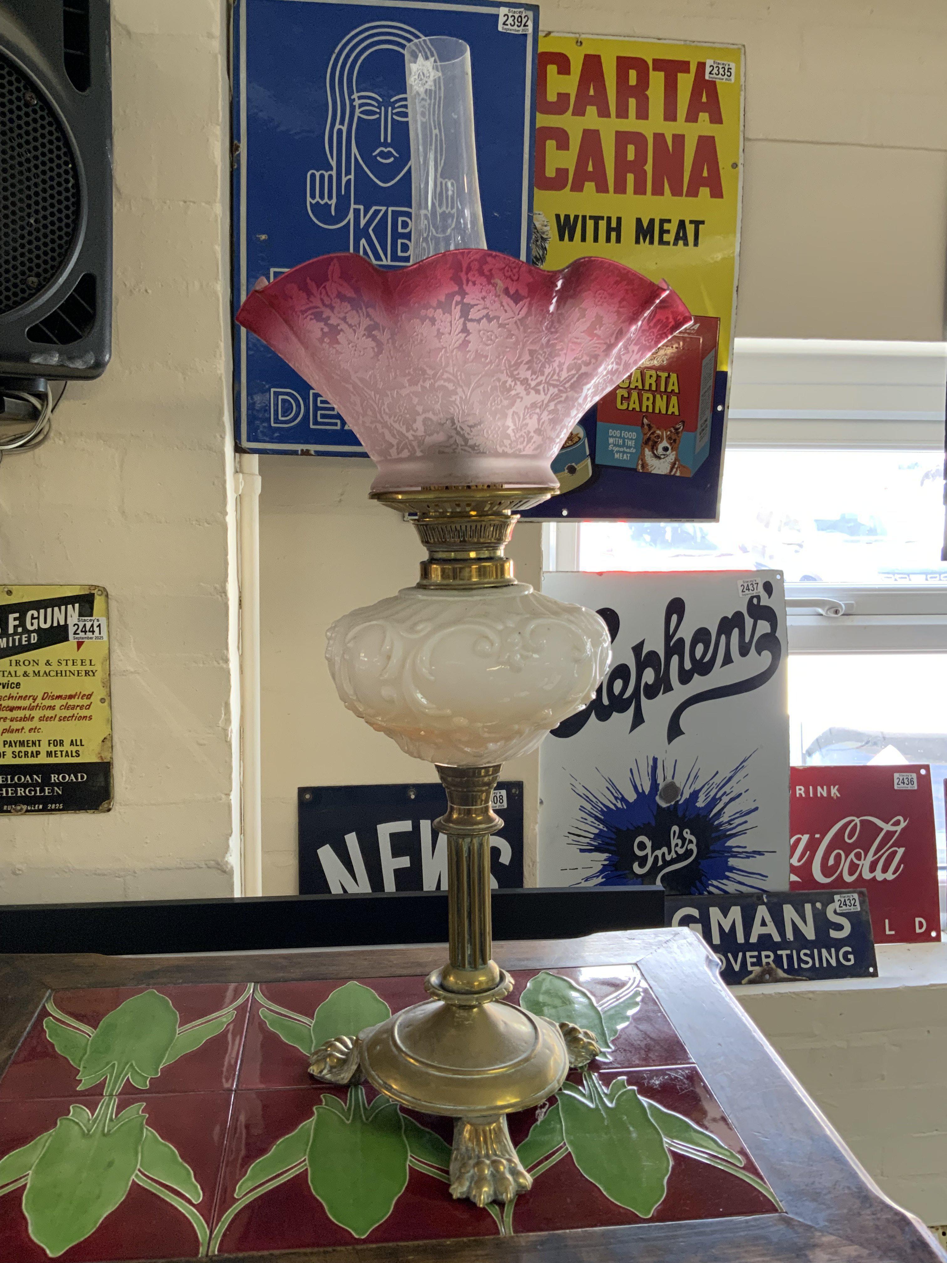 A Victorian brass column oil lamp with lion paw feet, opaline glass reservoir and faded etched cranberry shade.