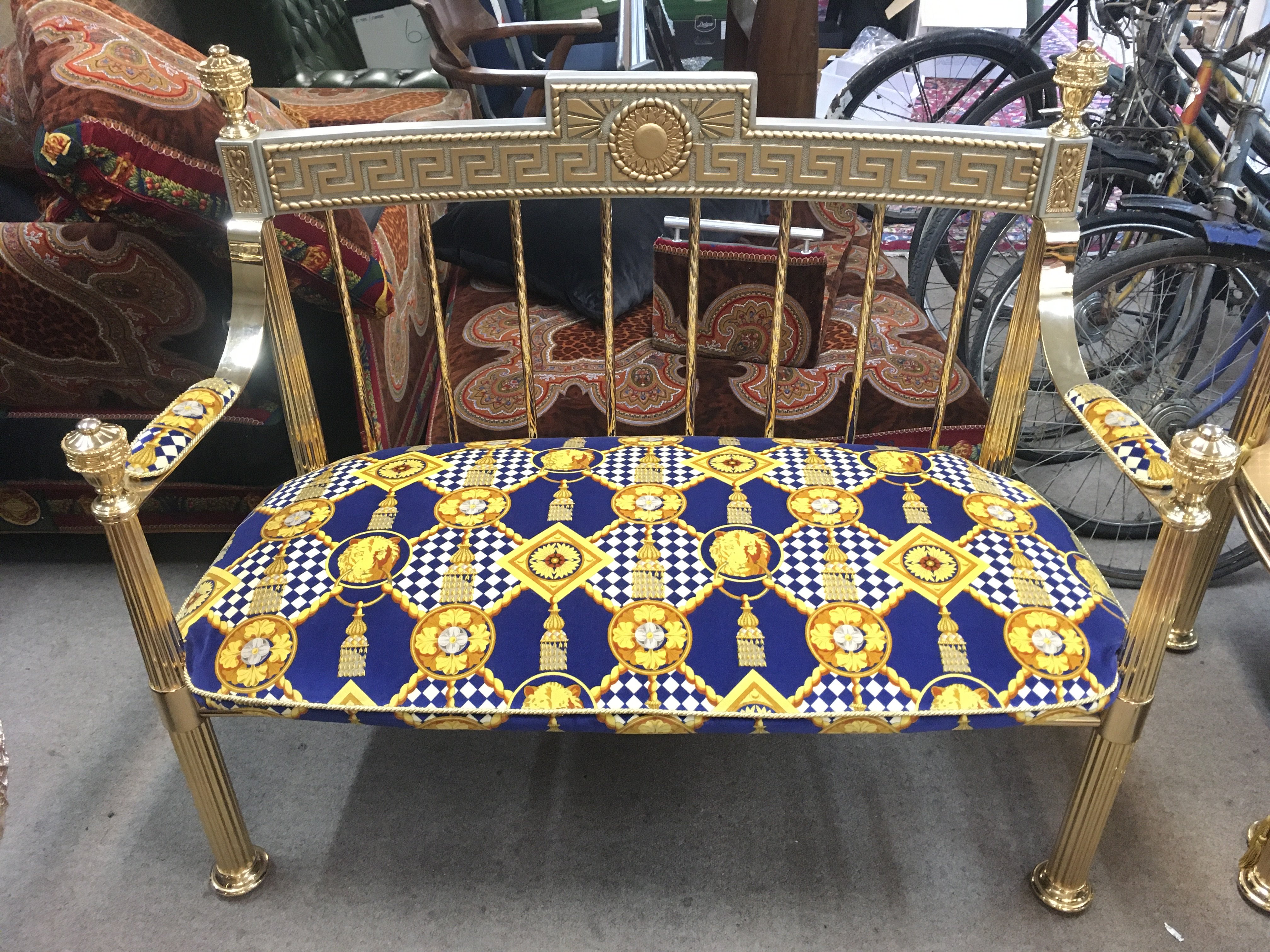 A Versace-style gilt settee upholstered in a blue, gold, and white Lion head-patterned fabric. With three pillows. 88cm tall, 118cm wide , 62cm long