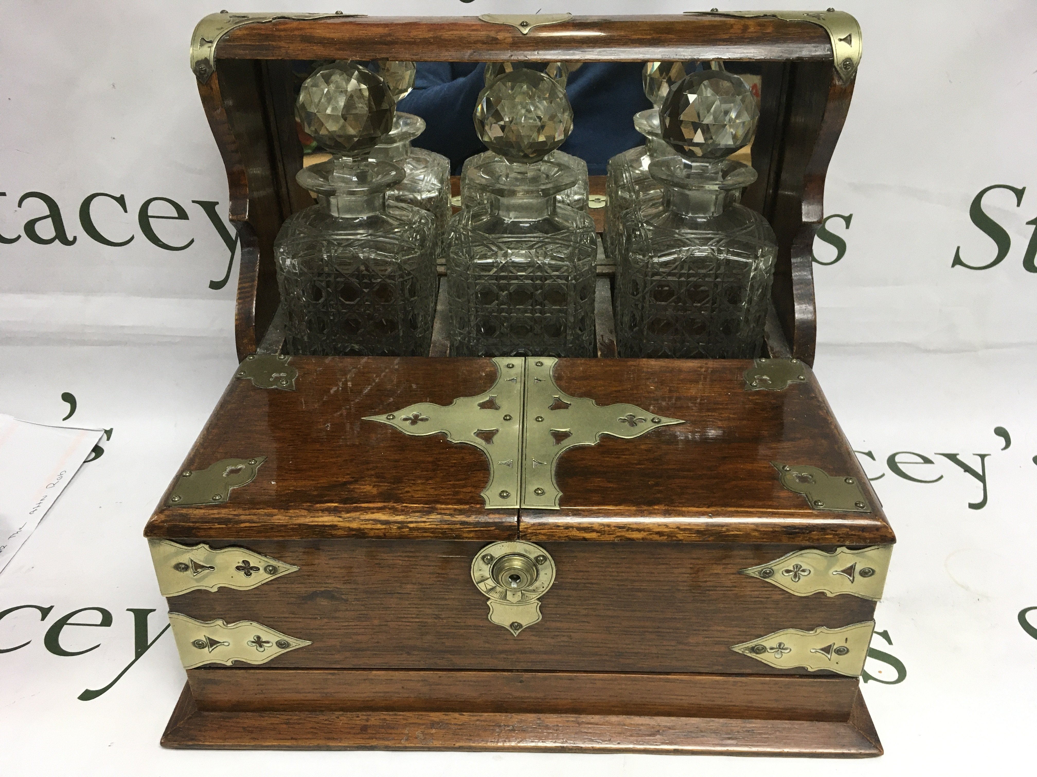 An oak tantalus with three bottles, no key but is open. Shipping category D.