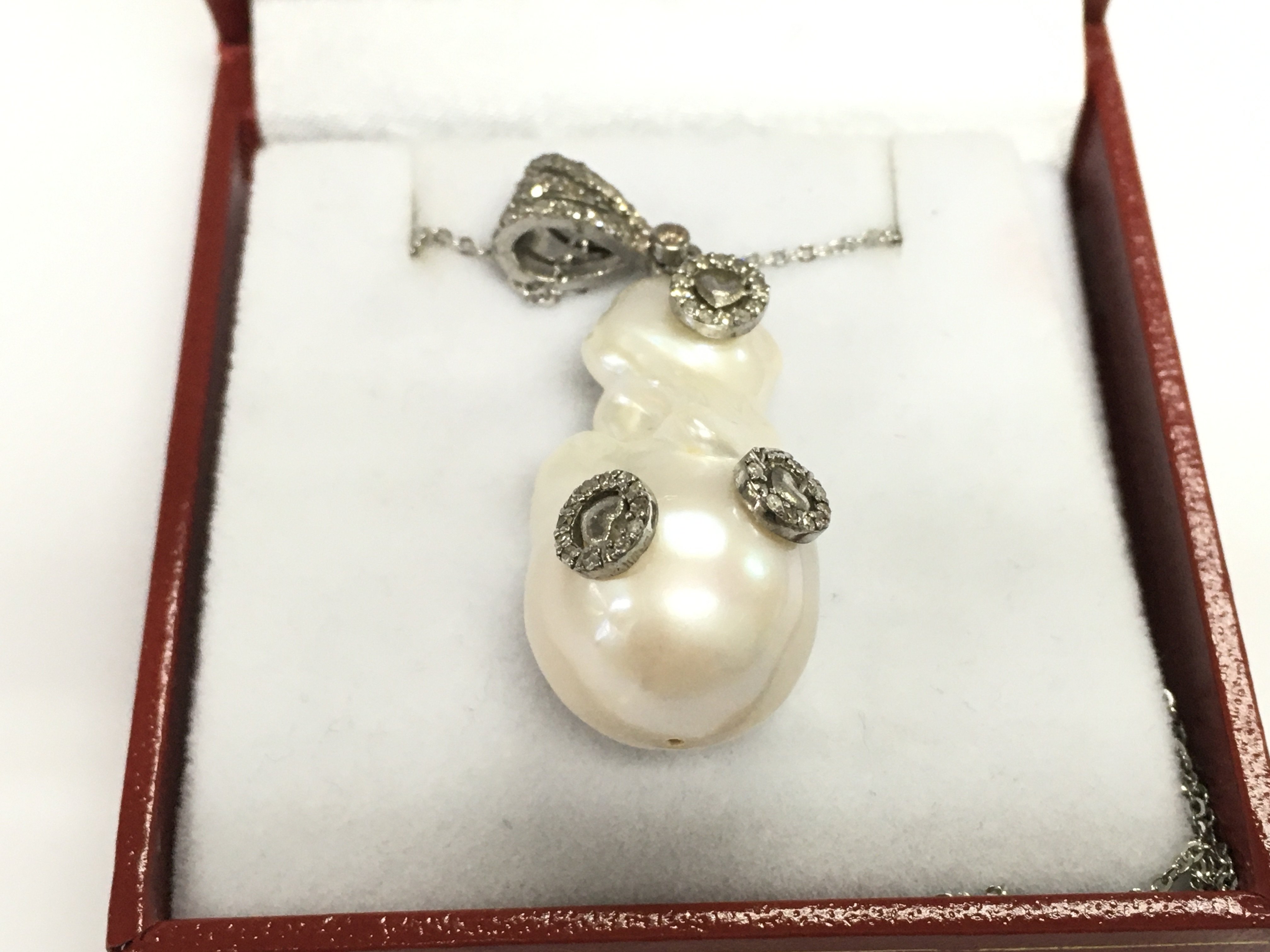 An unusual silver baroque pearl and diamond set pendant with heart motifs on a silver chain. Pearl 40.95ct and diamonds 0.32ct Approx.