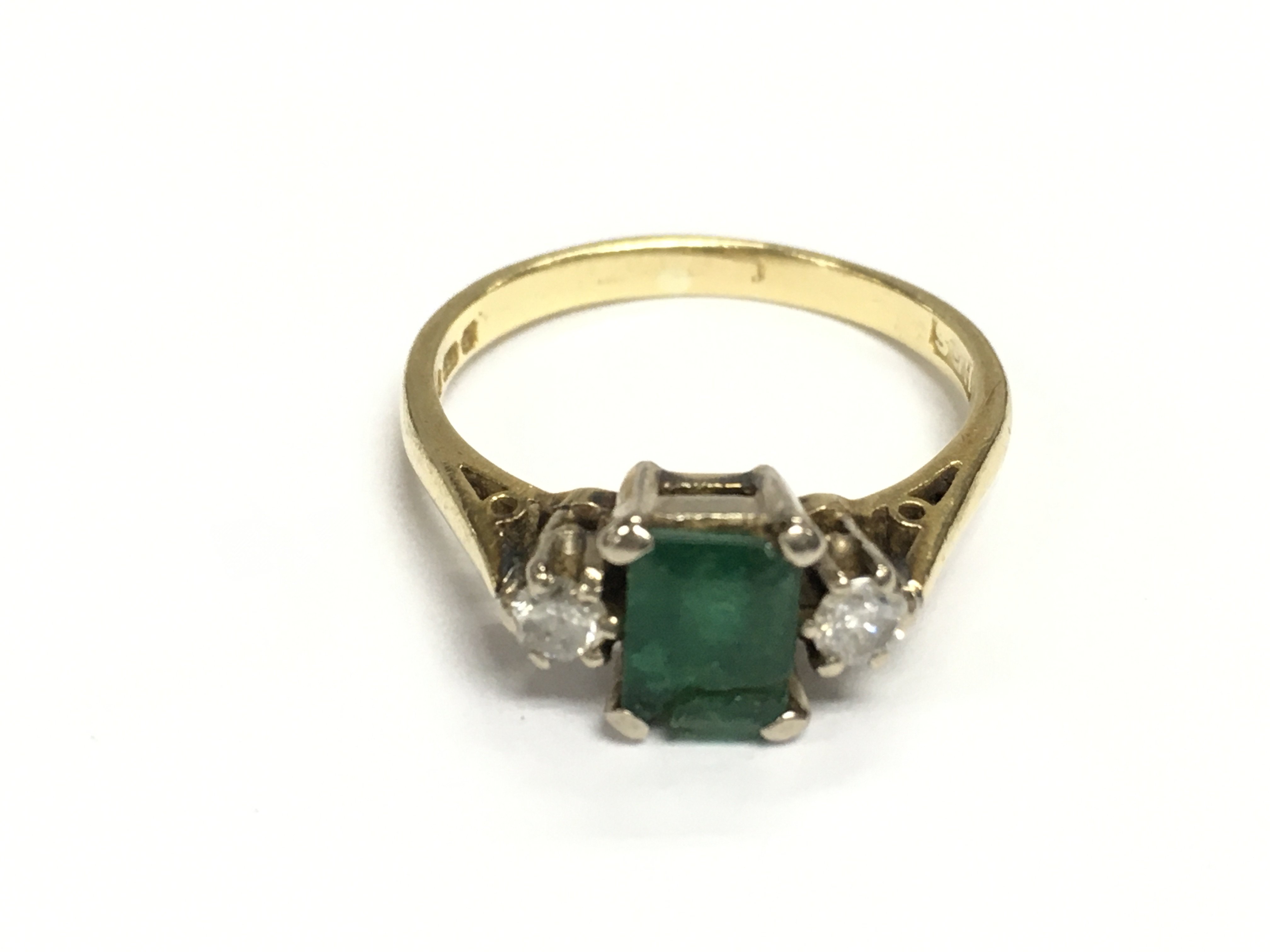 An 18ct gold ring set with central emerald and two diamonds. Size O and 3.59g Postage A