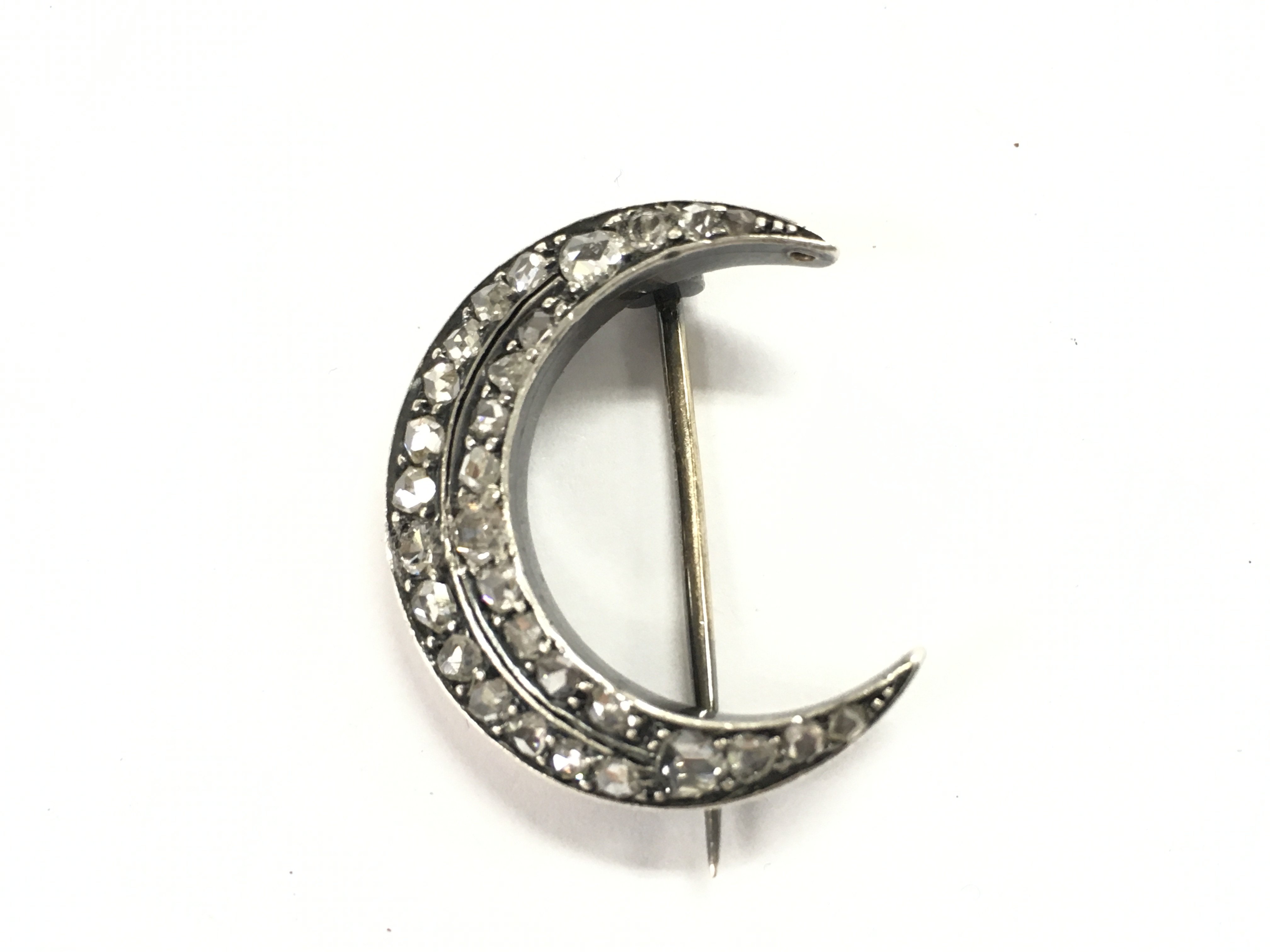 An unmarked silver and gold diamond set crescent brooch.