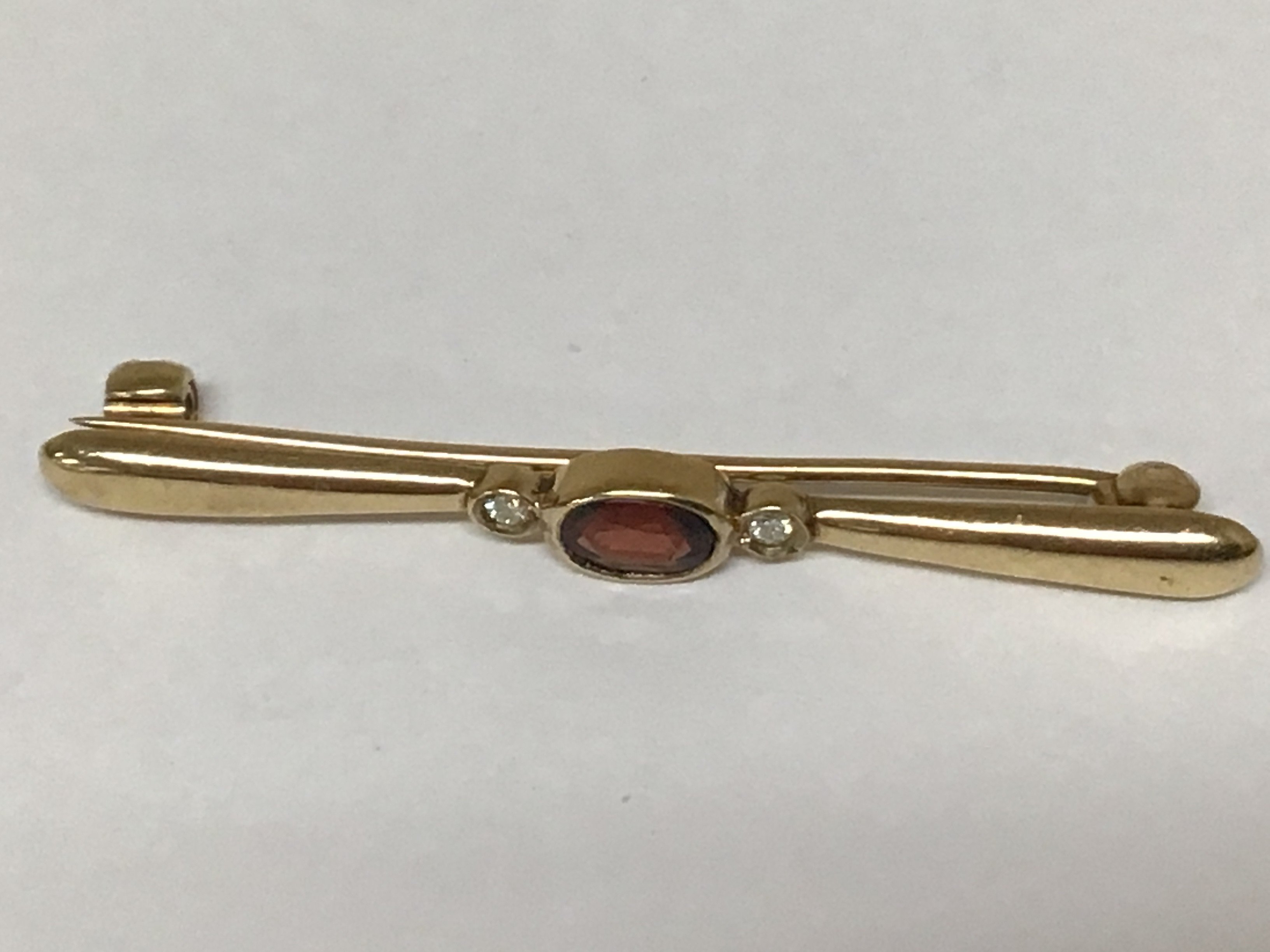A 9carat gold bar brooch set with a garnet flanked by small diamonds.weight 2.8g