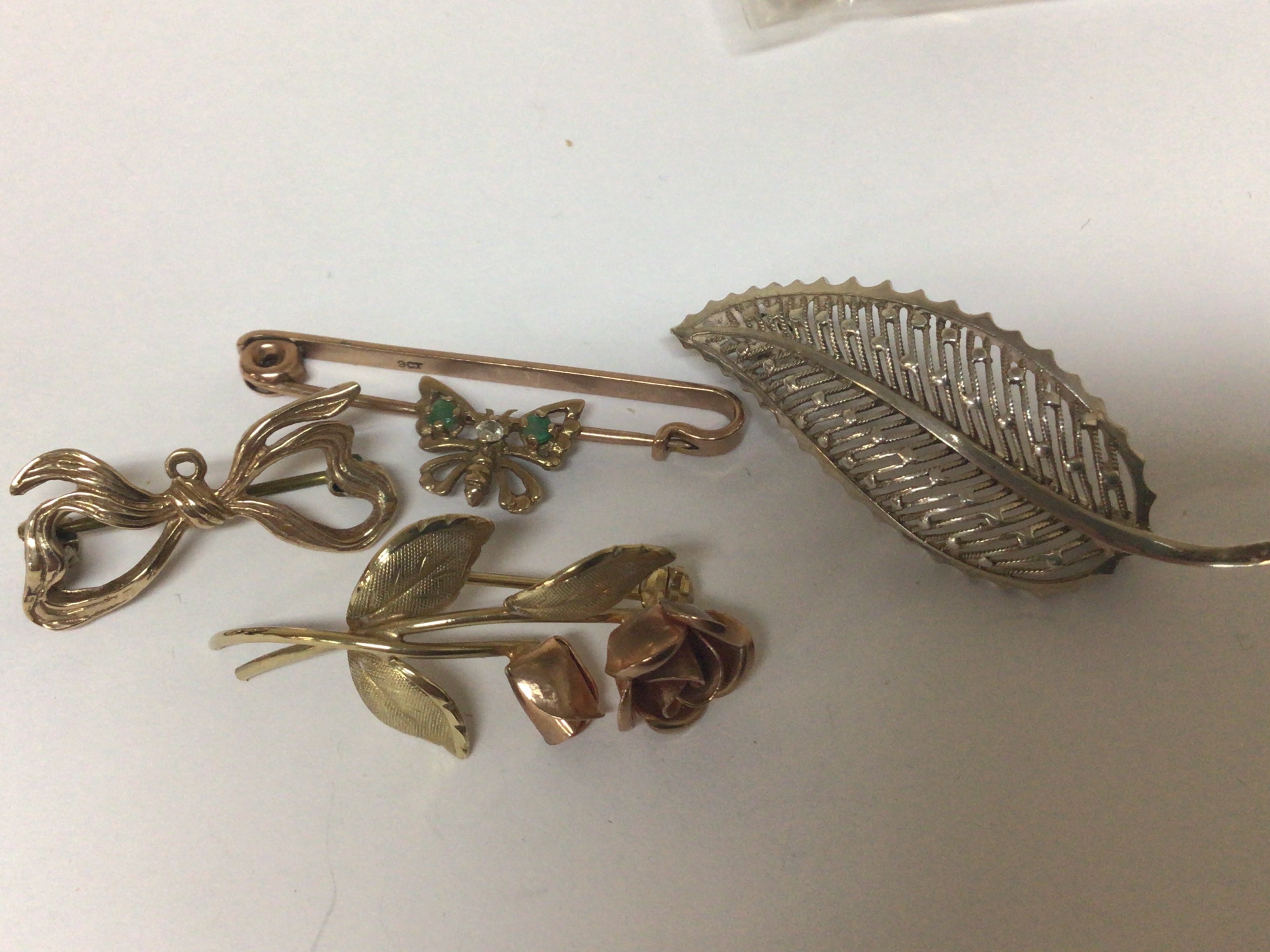 Three small 9carat gold brooches a ribbon tie small butterfly flowers weight 7g and one other brooch marked 935.