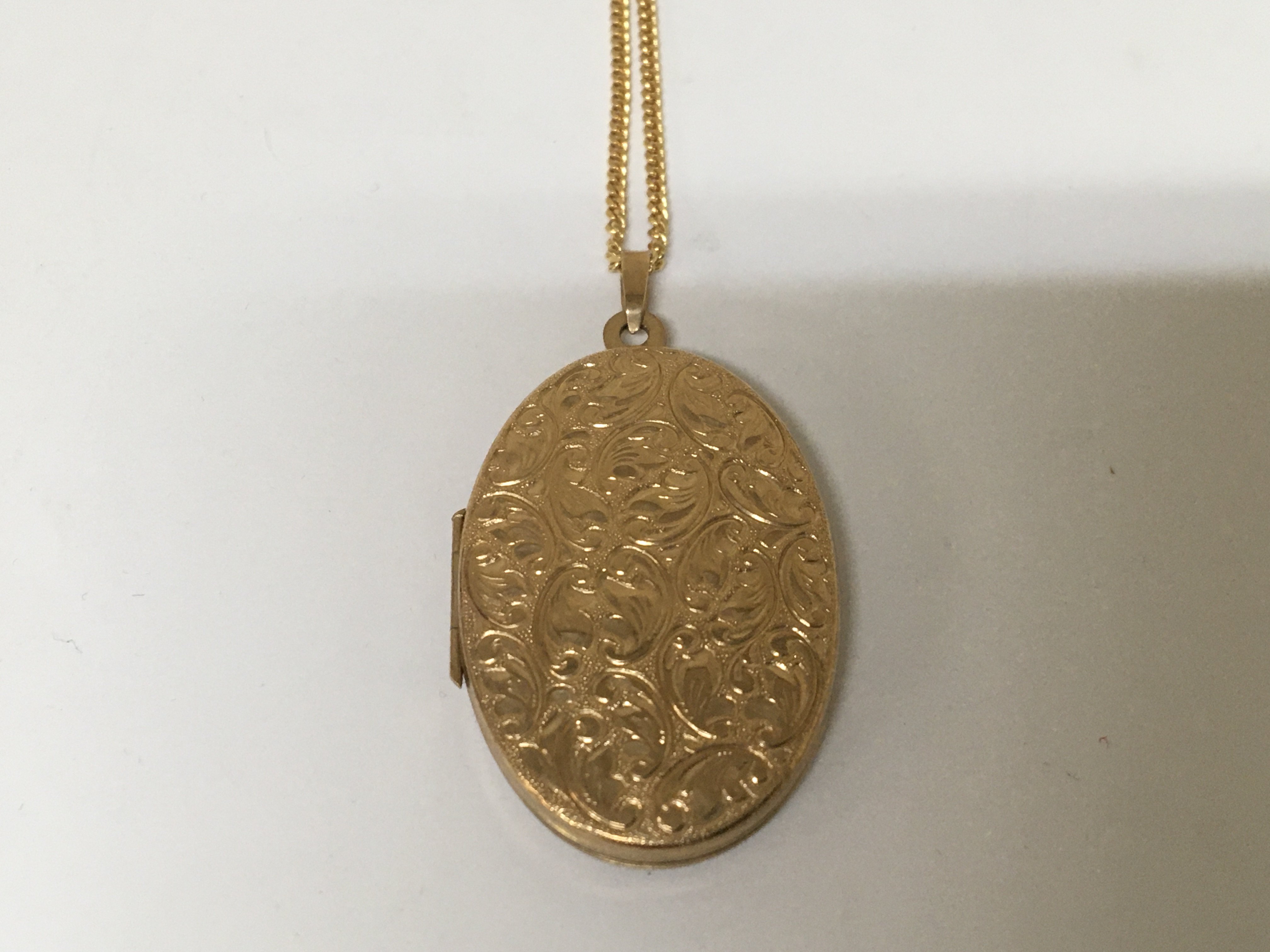 A 9carat gold oval locket with engraved scrolls with attached 9carat gold chain. Weight 8g