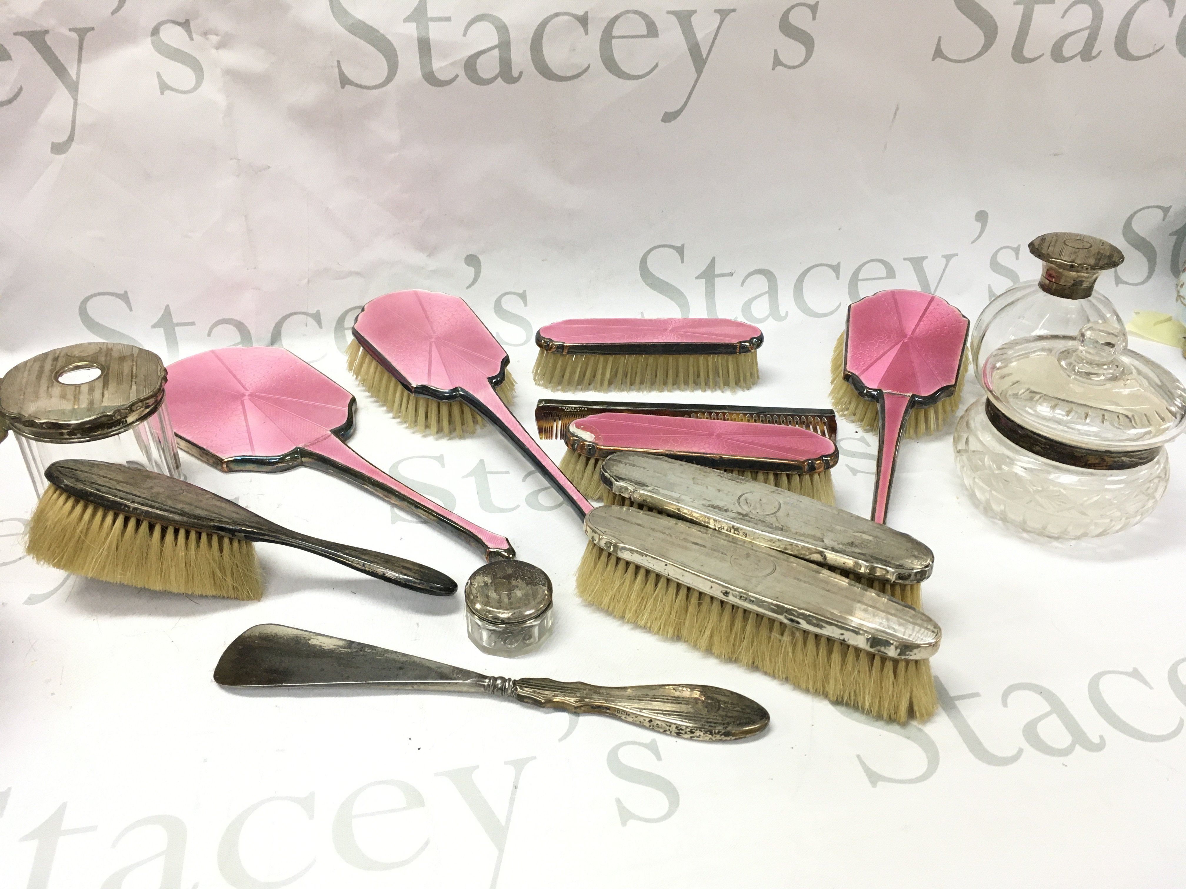 Silver hallmarked dressing table set including brushes, glass containers with silver collar, lids and a non silver pink enamel set . Postage category b