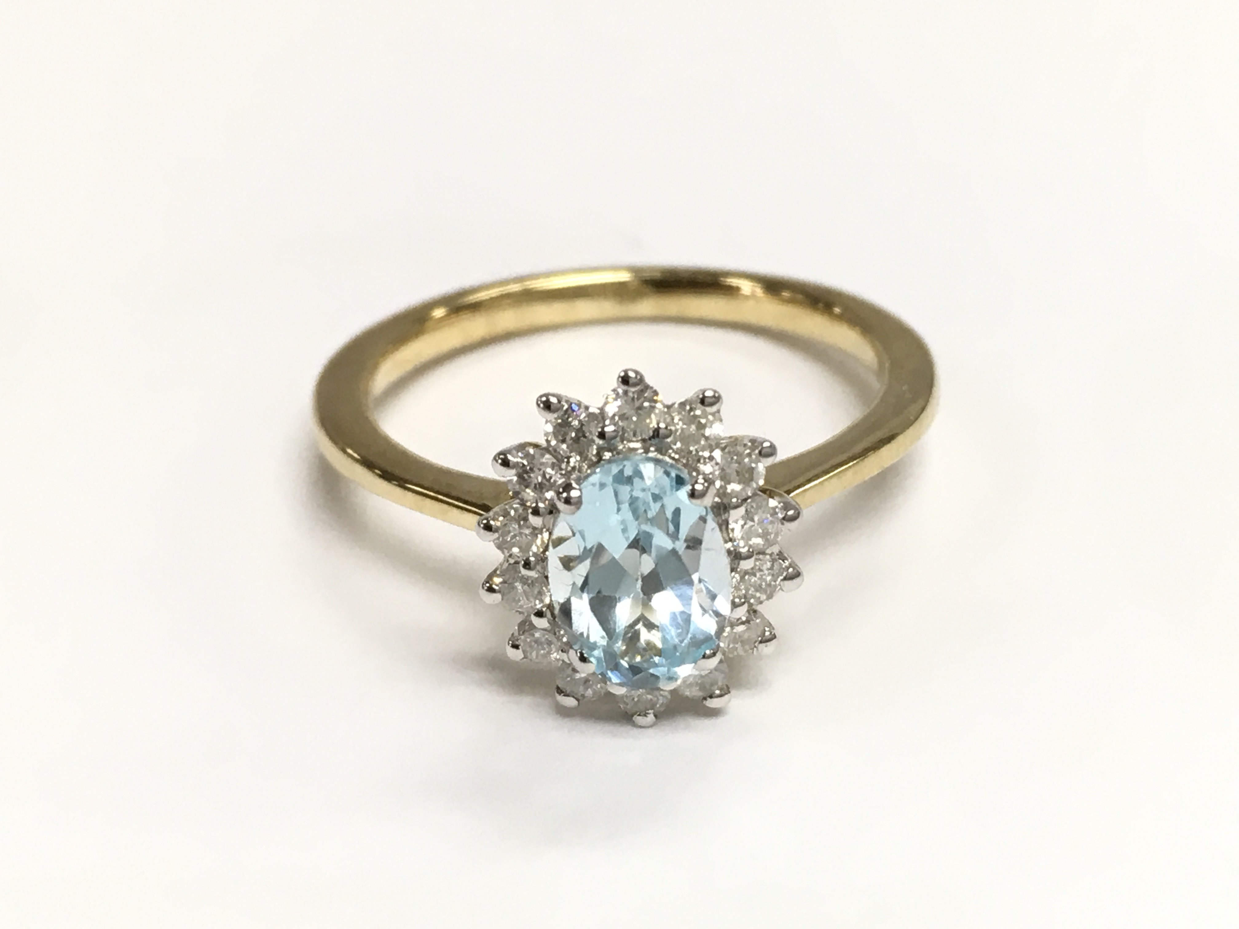 9ct yellow and white gold oval cut blue topaz and diamond cluster ring. Topaz 0.94ct and diamonds 0.24ct approximately. Size M