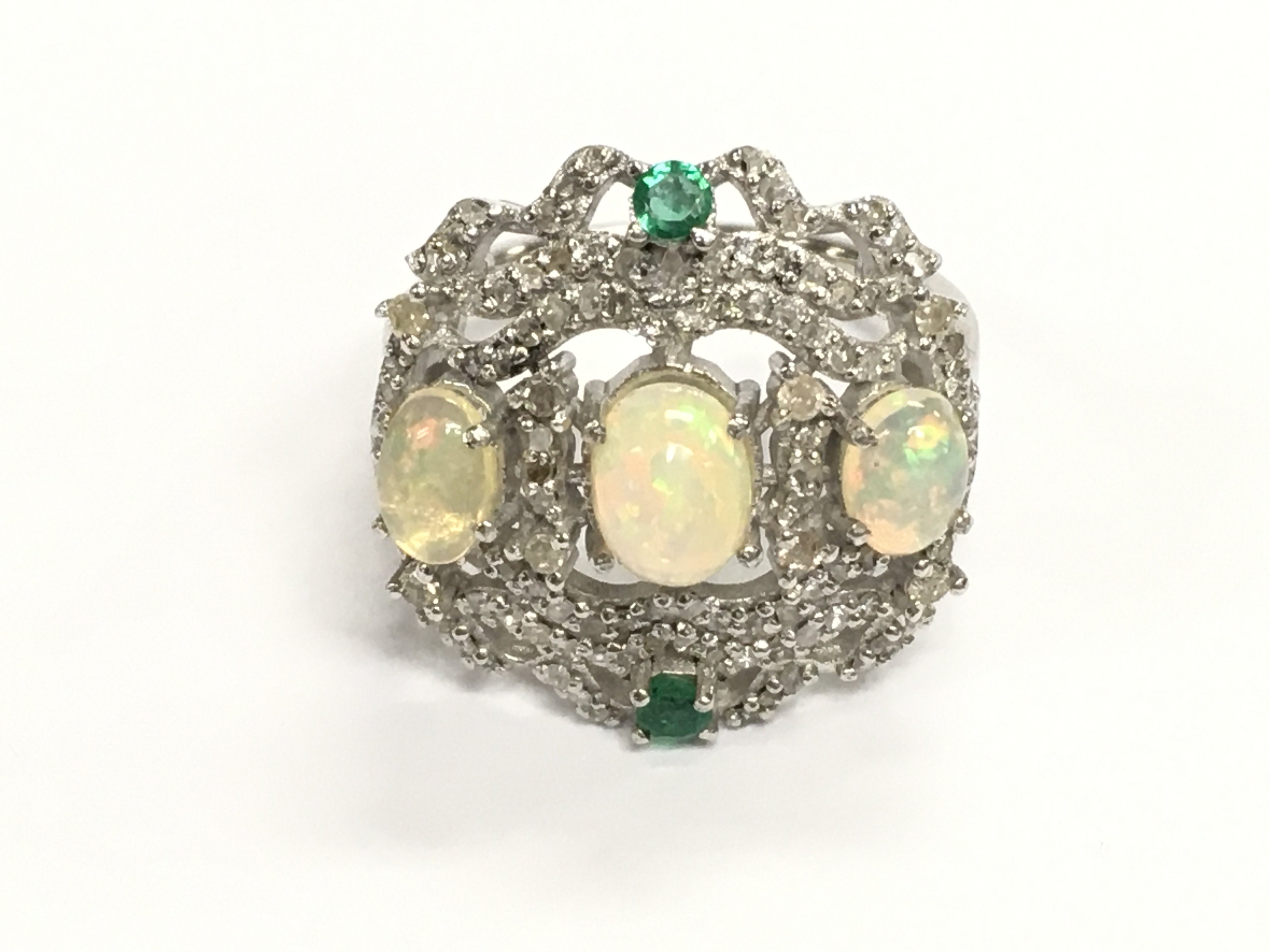 Ornate silver dress ring set with 3 oval cabochon opals 2 emeralds and diamonds. Approximately 1.80ct opal 0.15ct emerald and 0.35ct diamonds. Size P 1/2