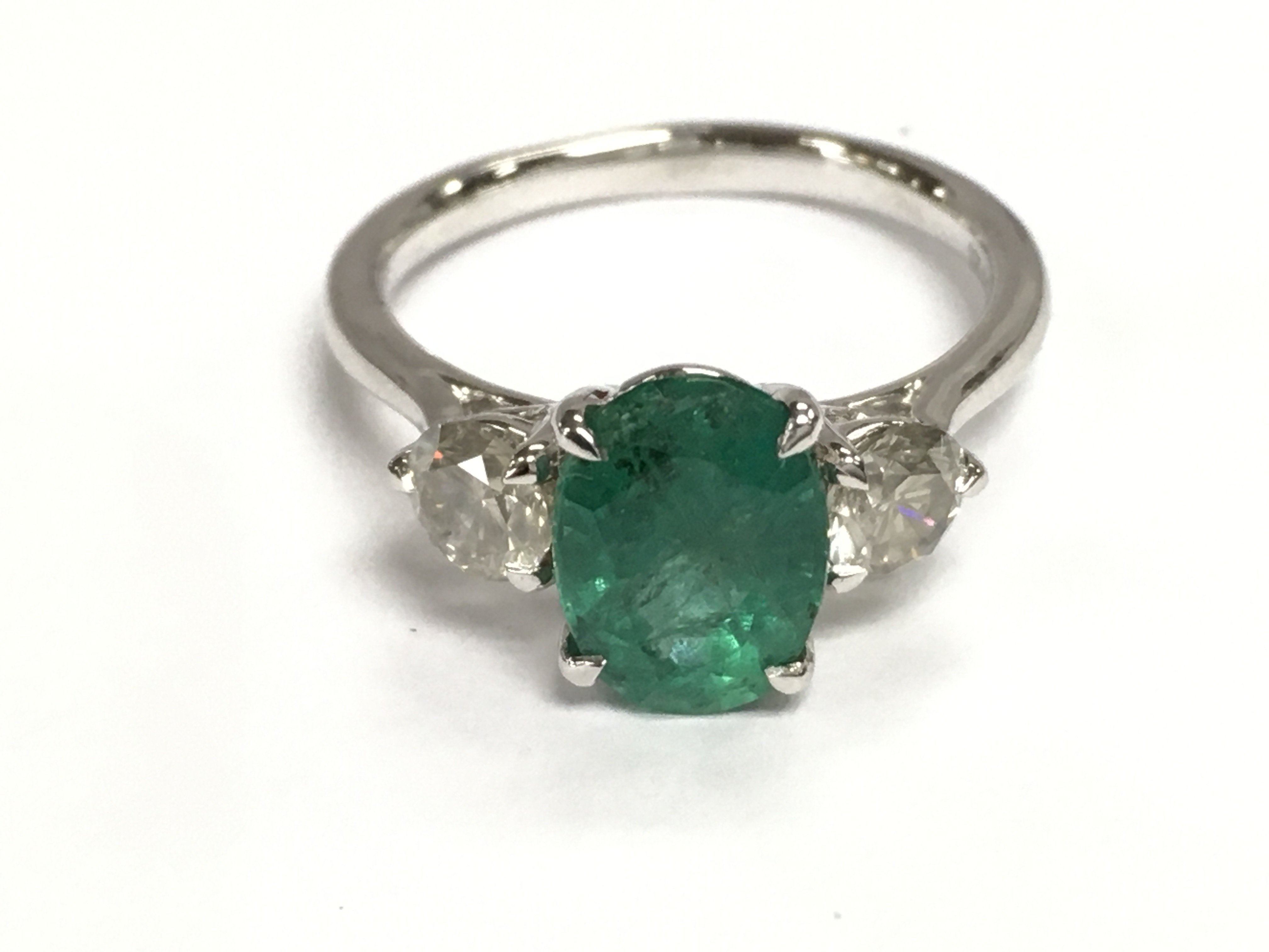 A platinum trilogy ring set with central oval emerald flanked by two diamonds. Emerald 1.94ct and diamonds 0.73ct approximately. Size N