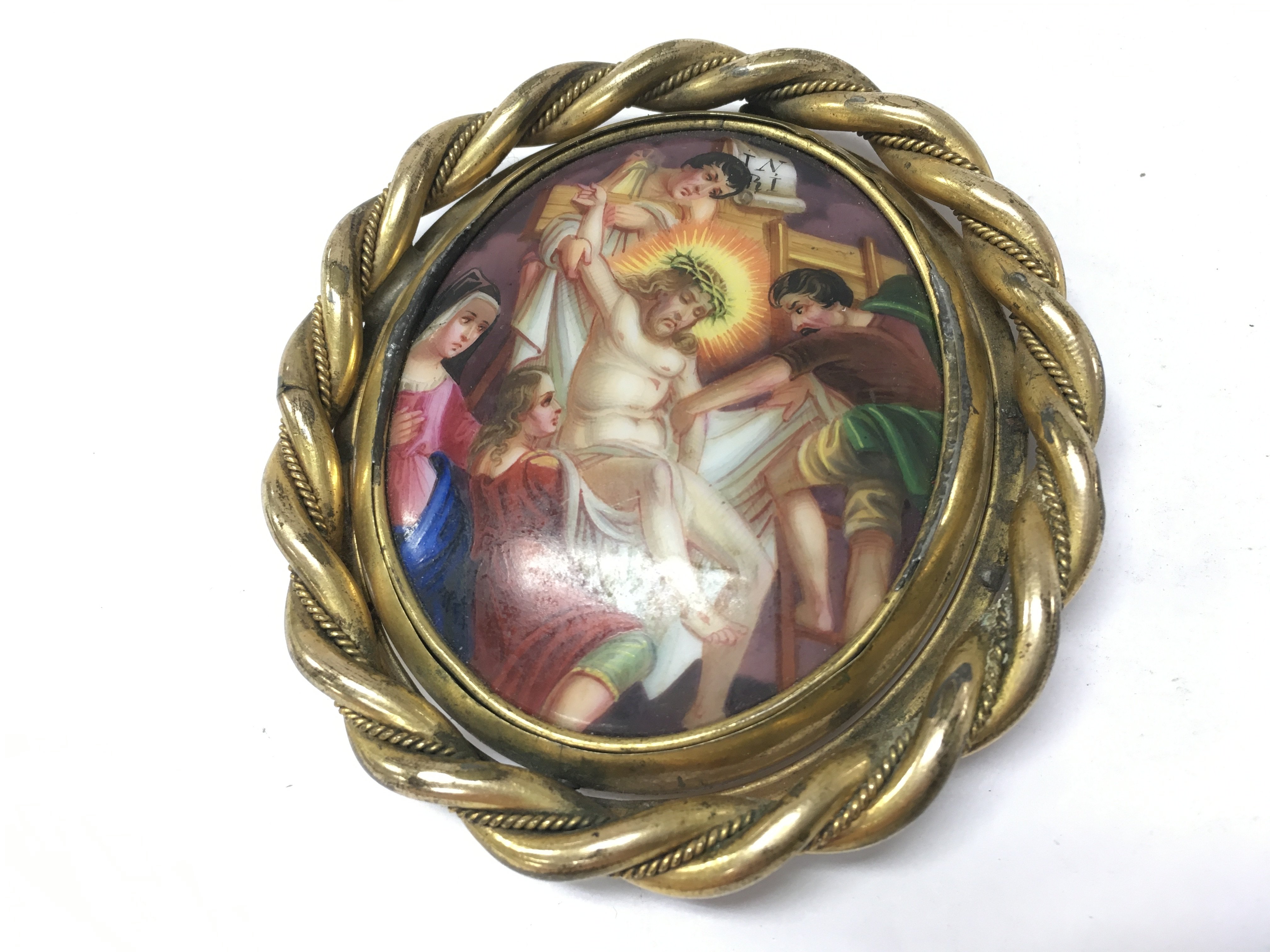 A porcelain hand painted Religious brooch depicting Jesus being taken down from the cross.