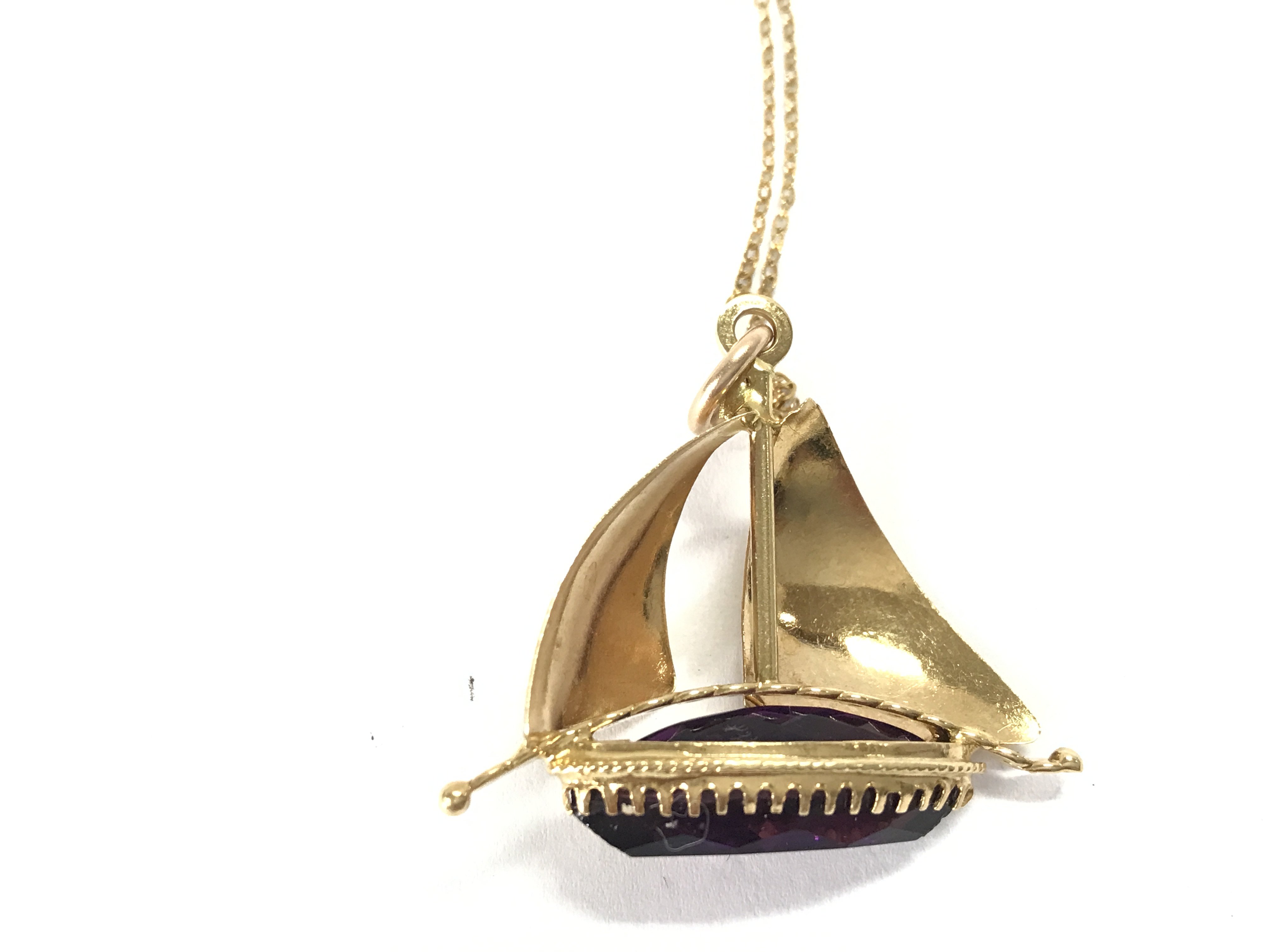 An 18ct gold pendant in a ship design set with an amethyst on chain. 7.70g Postage B