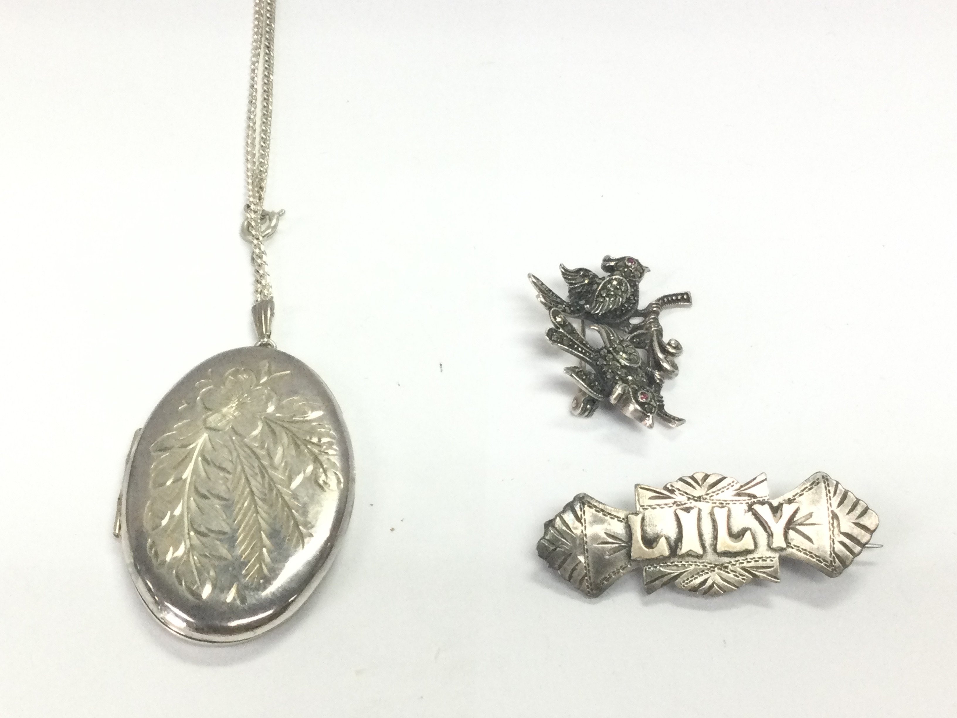 A silver locket on silver chain along with two silver brooches. 23.18g Postage A
