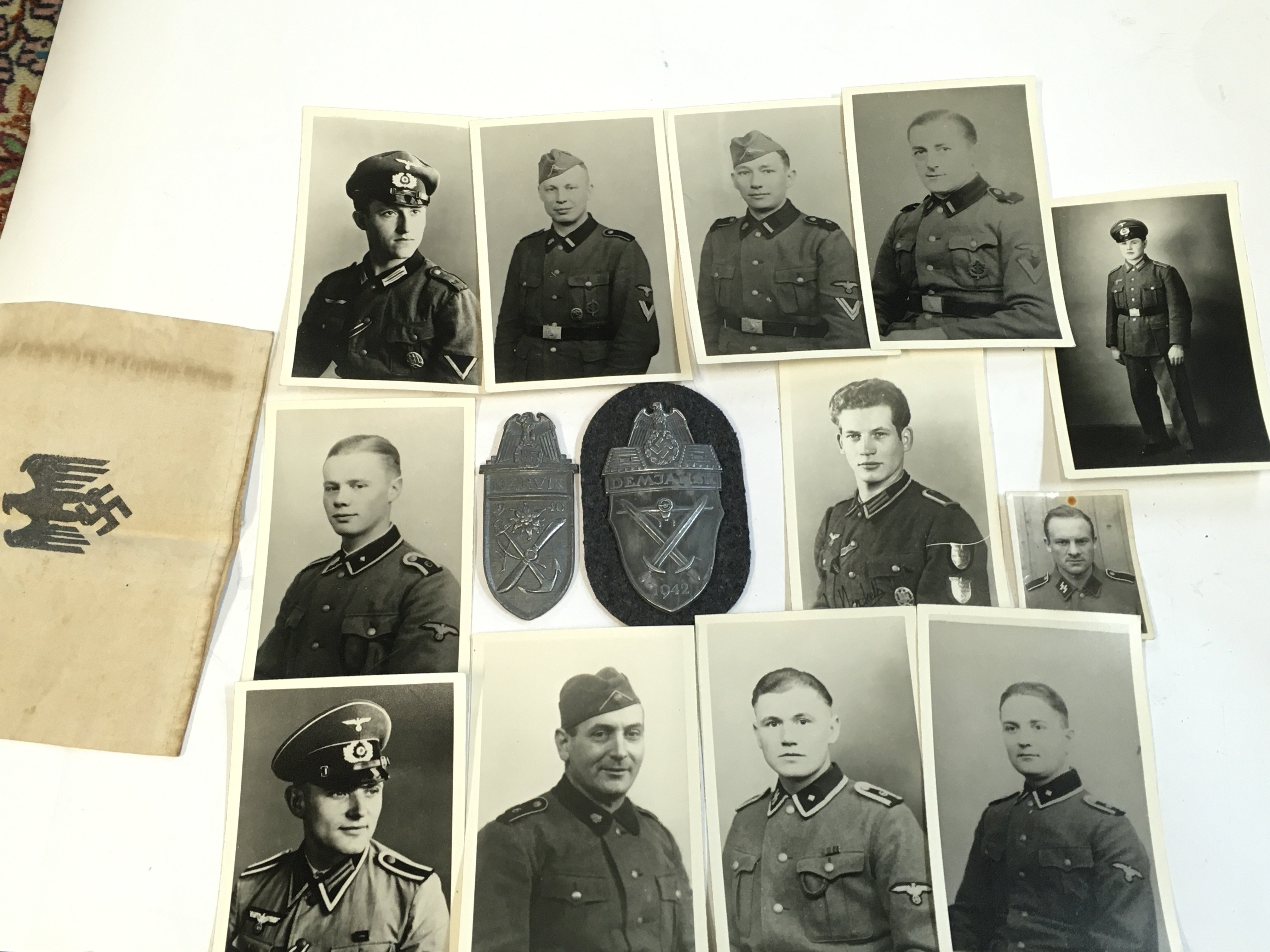 An assortment of German photos , German armband , Navrik arm shield, Demansk arm shield and a gas mask container .Postage cat a