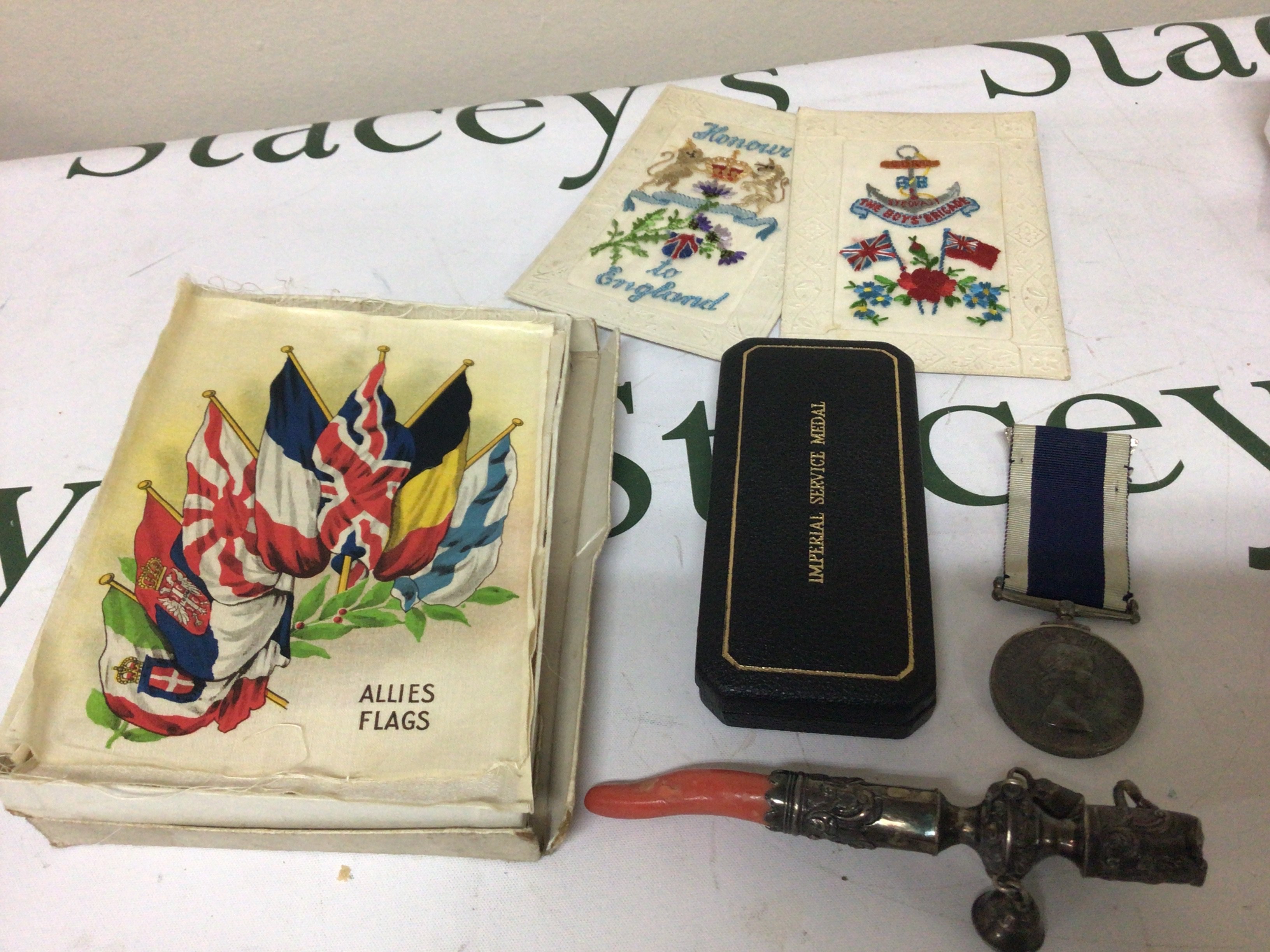 An Antique Silver Childs rattle with applied coral a collection of silk large size flags Allies Flags by BDV cigarettes two I world war silk post cards An Elizabeth II Long Service and good conduct medal Mx 849933 LS Rowe PO CK HMS Jaguar. and an Imperial Service Medal George VI.