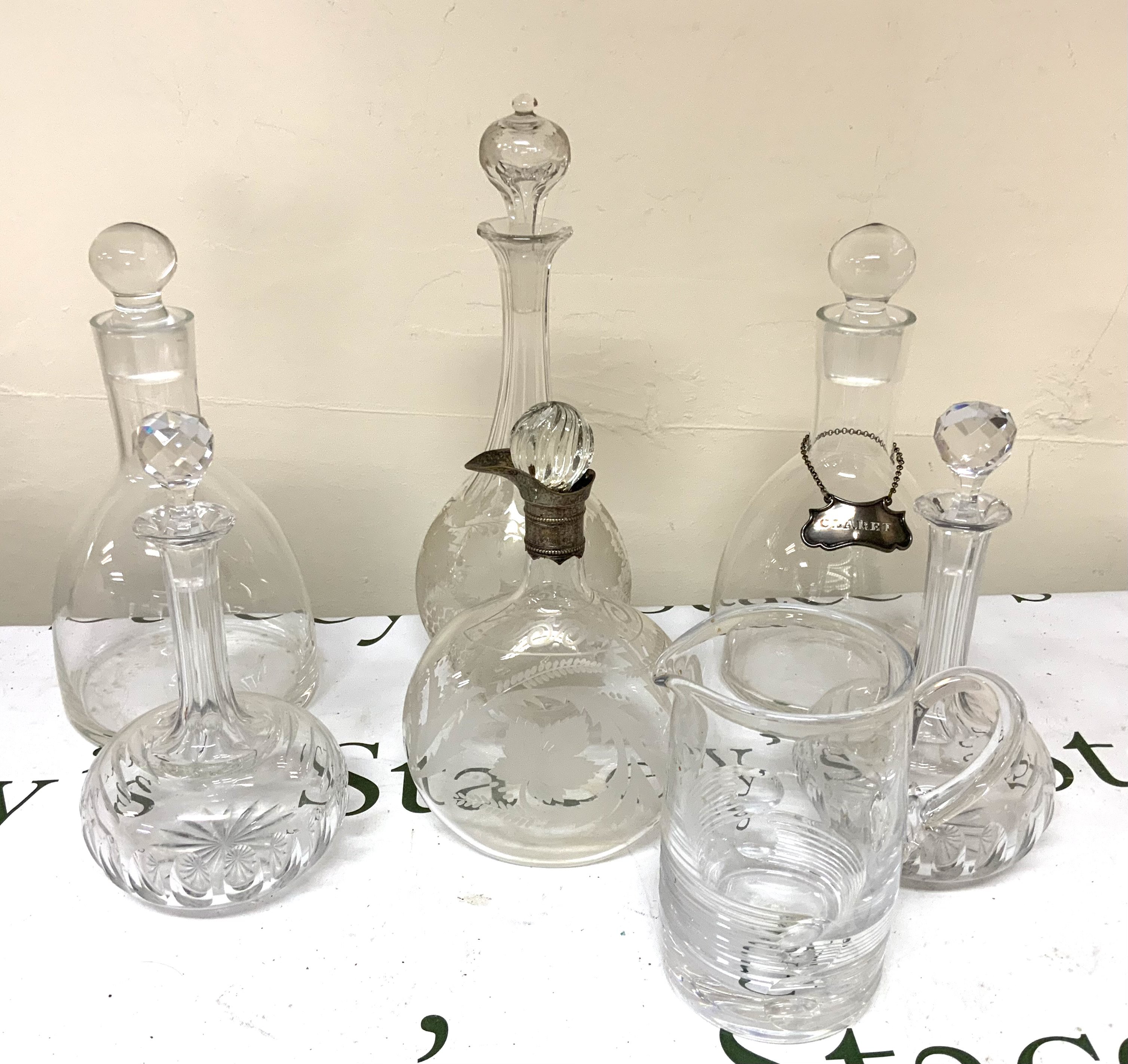 A pair of Blown glass claret jugs, a tall sherry decanter with etched floral decoration, A pair of Edwardian cut glass claret jugs, A Victorian floral etched whisky decanter with silver plated spout collar (later stopper), Atlantis cut crystal water jug.