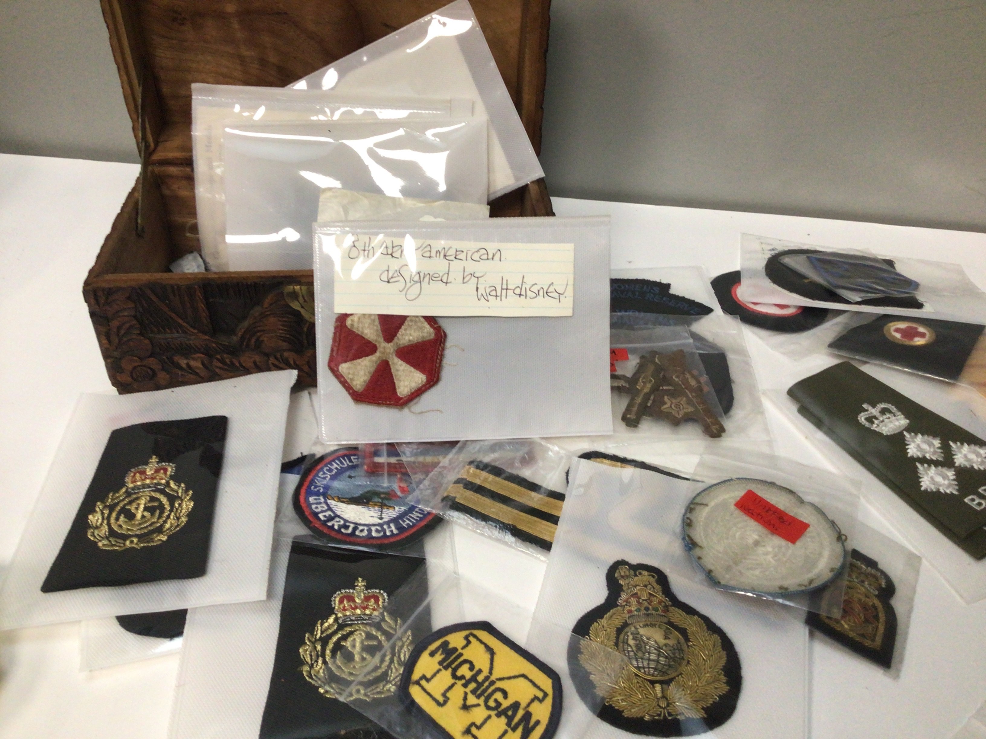 A small carved camphor wood trunk containing a quantity of cloth military badges including American badges
