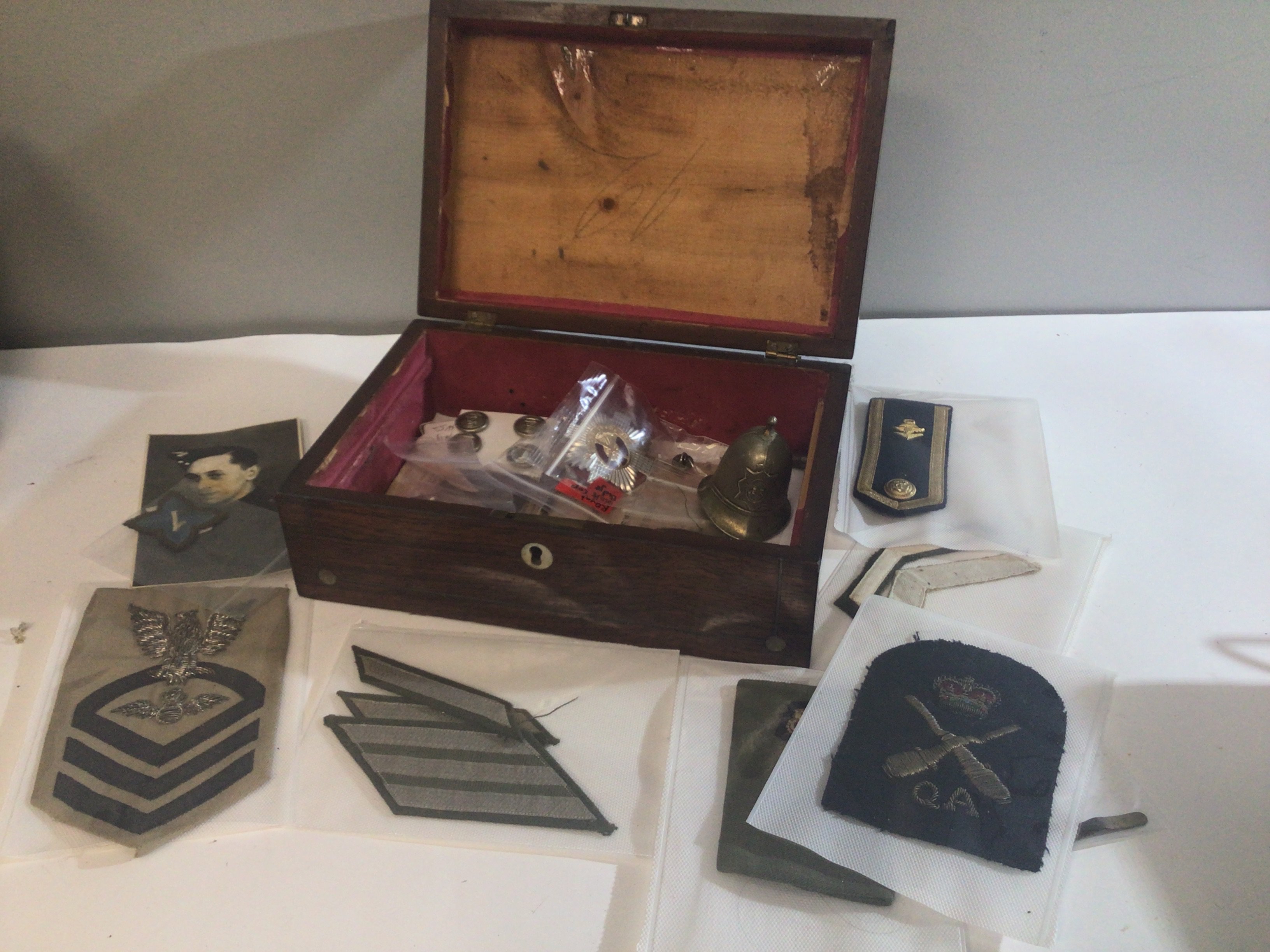 A Rosewood box containing Military cloth badges British and American other badges and a small helmet shaped bell.