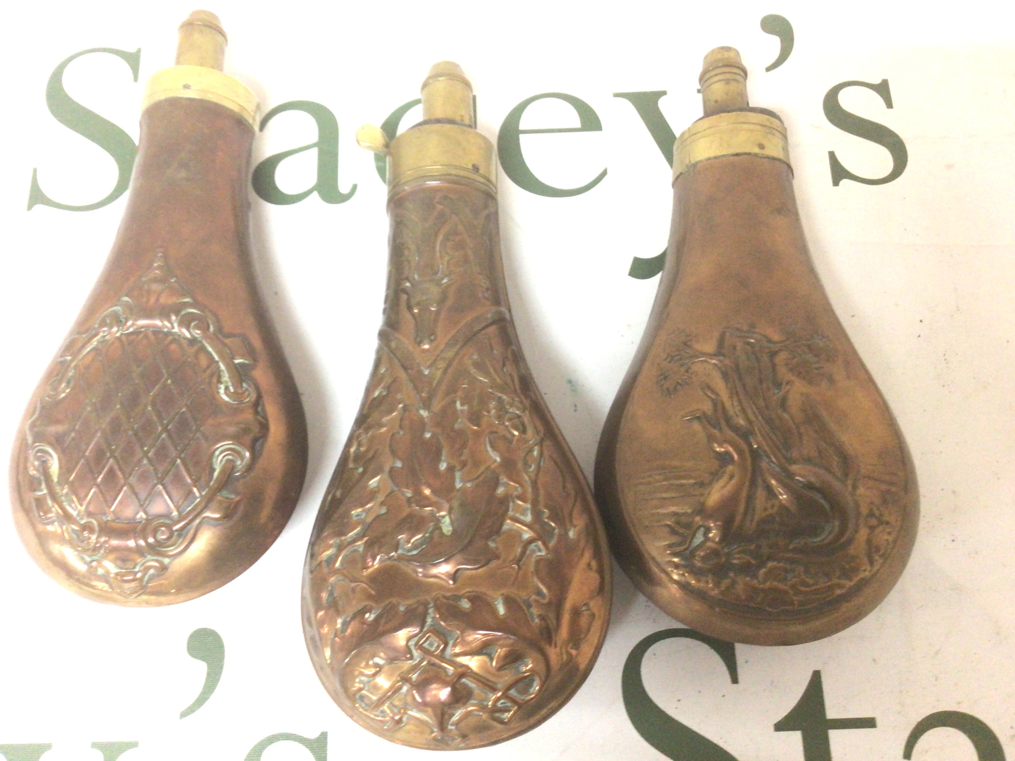 Three 19th Century copper powder flasks. Repousse chased decoration with game birds and brass mounts (3)