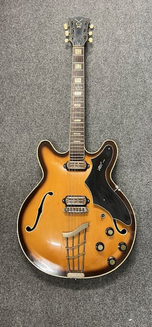 A 1964 Vox Lynx electric guitar. Semi sold thinline type with rosewood type board and block markers. This guitar comes with the rarer batwing pick guard and toaster style pickups. Being a circa 1964 guitar it was made in Italy at the Crucianella factory. Condition wise good considering age and use and has tarnishing to brightwork and some crazing in the lacquer which has aged to a nice patina. Comes with cardboard case.