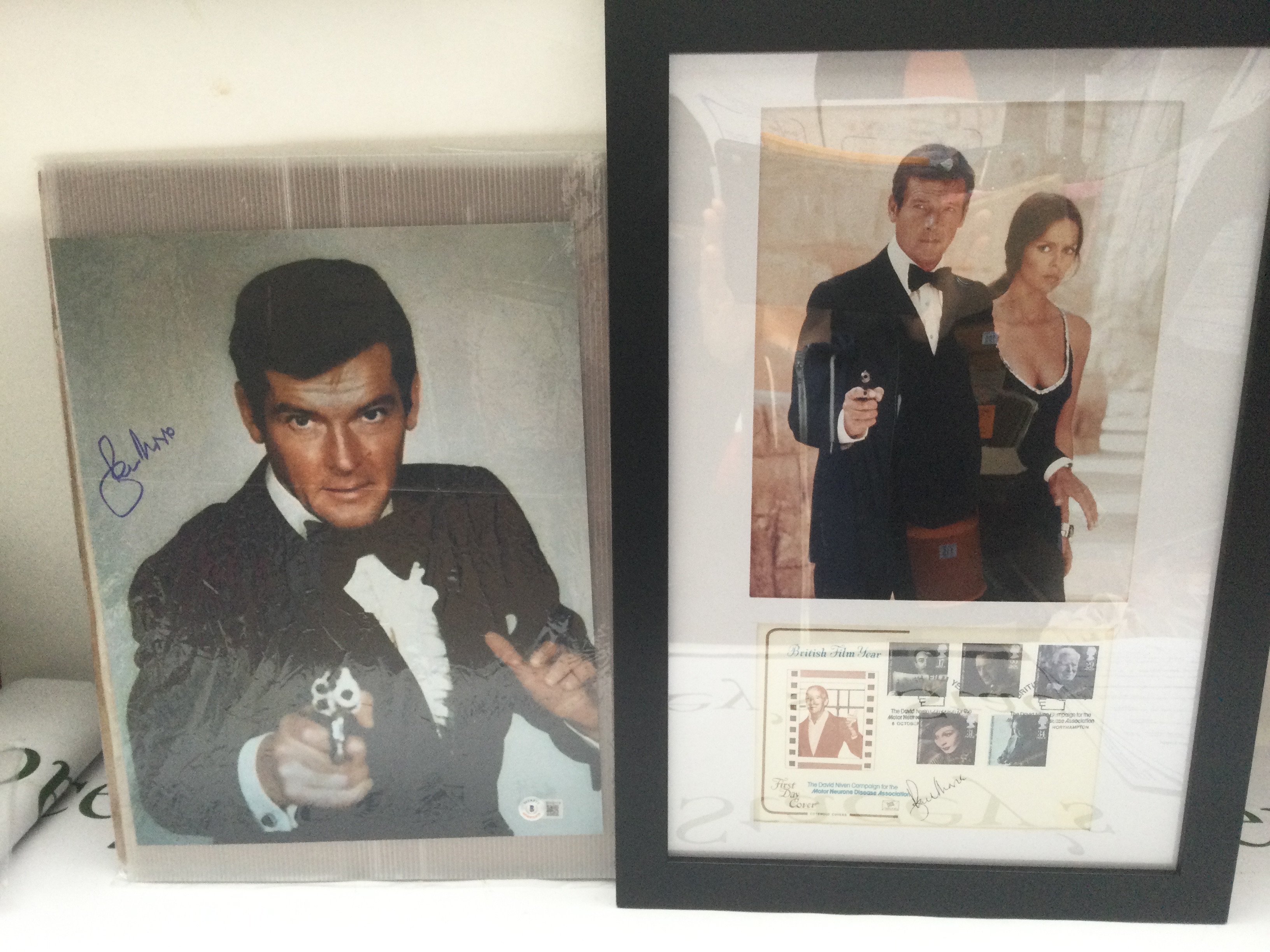 A James Bond photo signed by Sir Roger Moore, approx 27cm x 35cm with Beckett COA together with a framed and glazed First Day cover and photo display also signed by Moore (2).