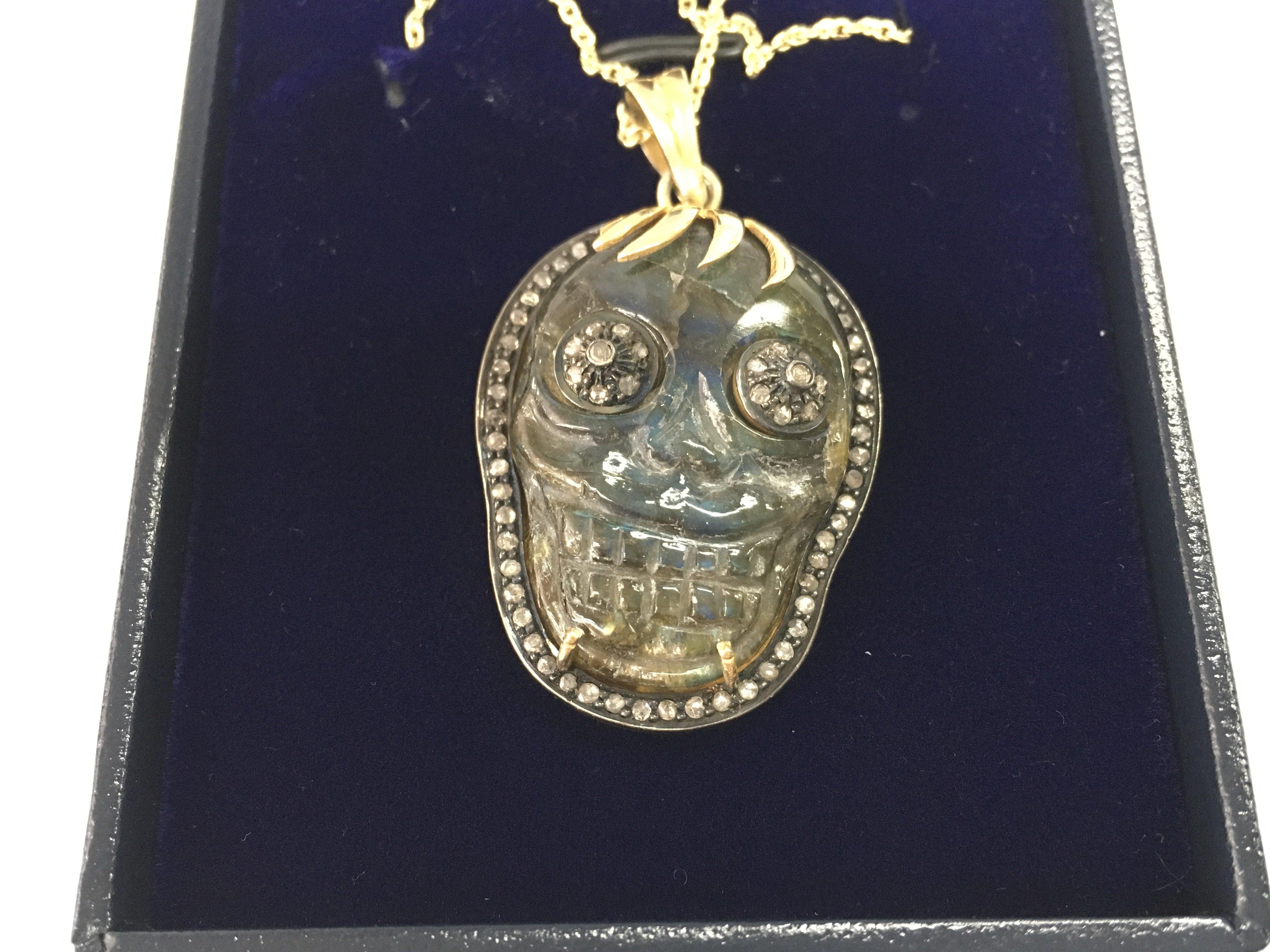 A large skull pendant in yellow metal with rose cut diamond set into a carved labradorite on a gold plated silver chain. Labradorite 37.55 and diamonds 0.81ct. Postage B