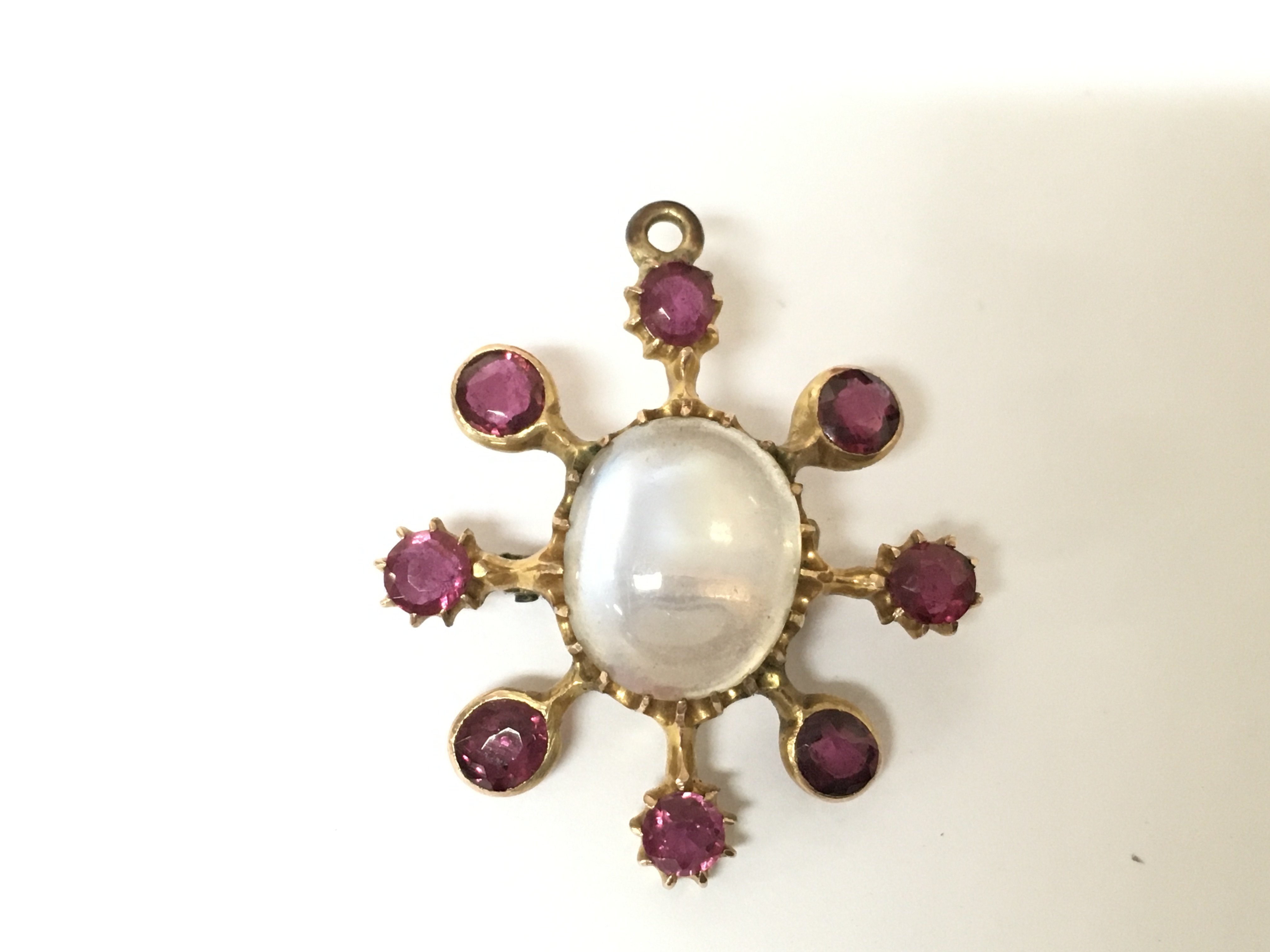 An unmarked yellow metal moonstone and ruby star brooch. 3.65g