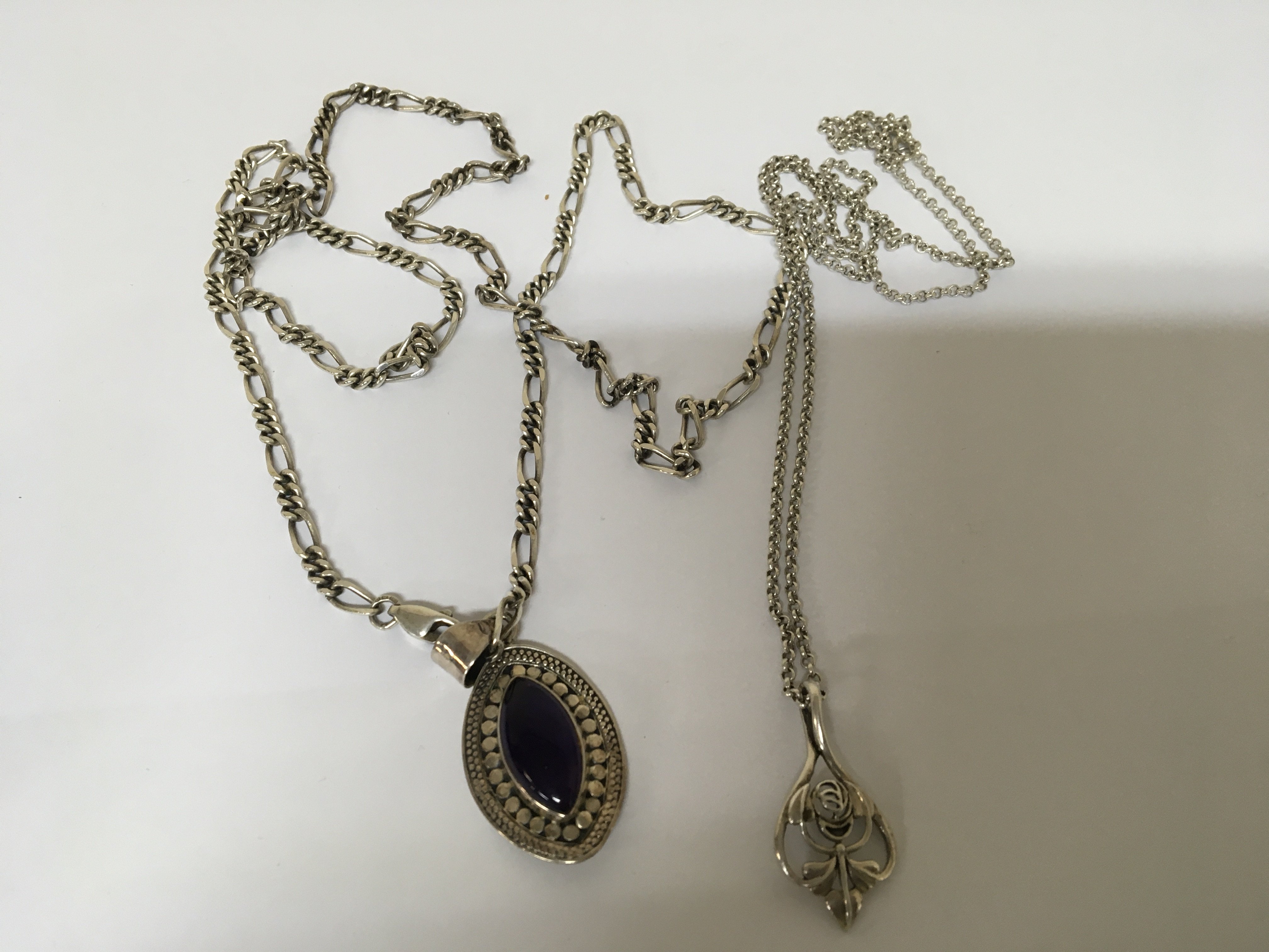 Two Silver necklaces one with a polished amethyst and one other floral pendent both on silver chains. (2)