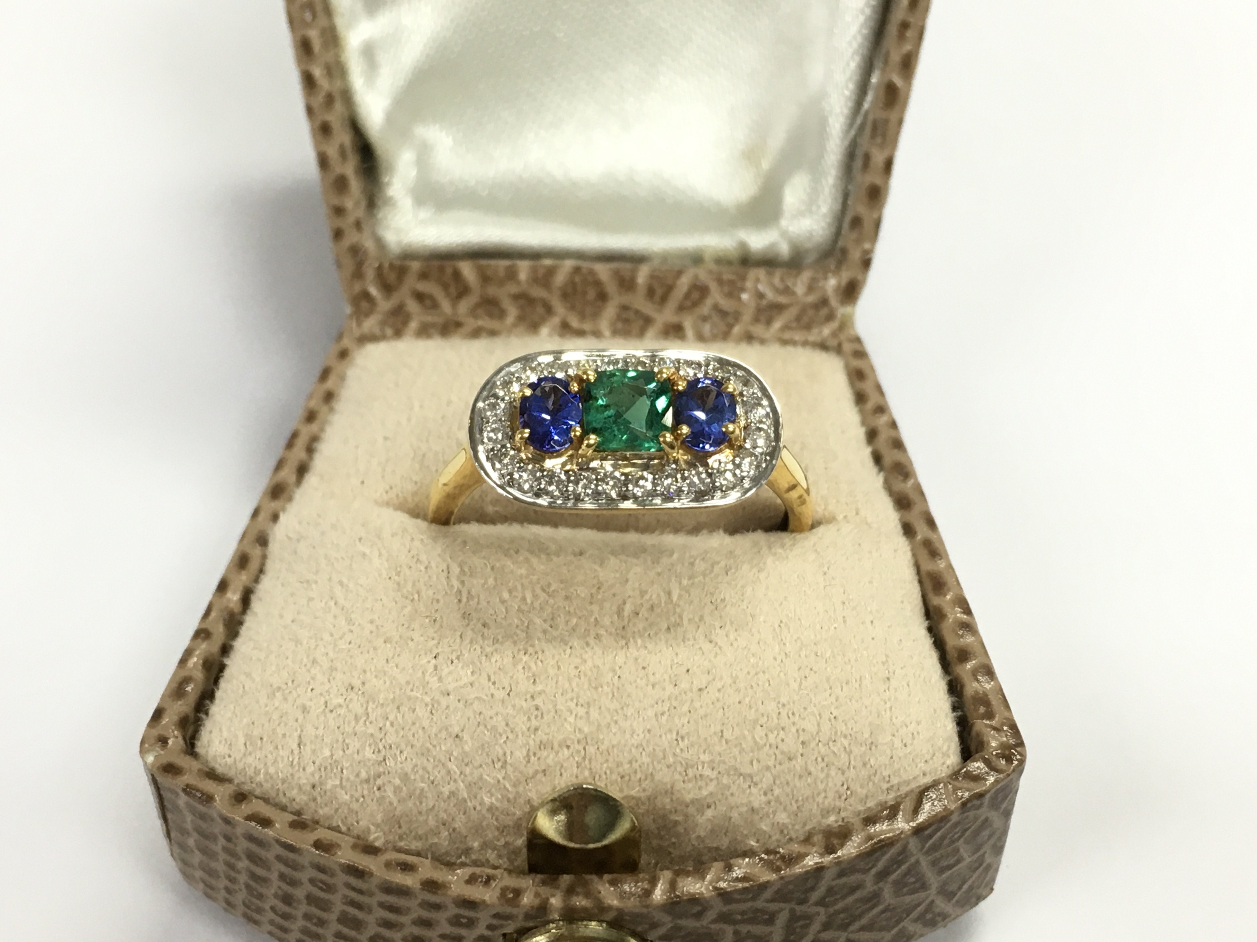 14ct yellow gold deco inspired ring set with a square cushion cut emerald and oval tanzanite surrounded by diamonds. Size P
