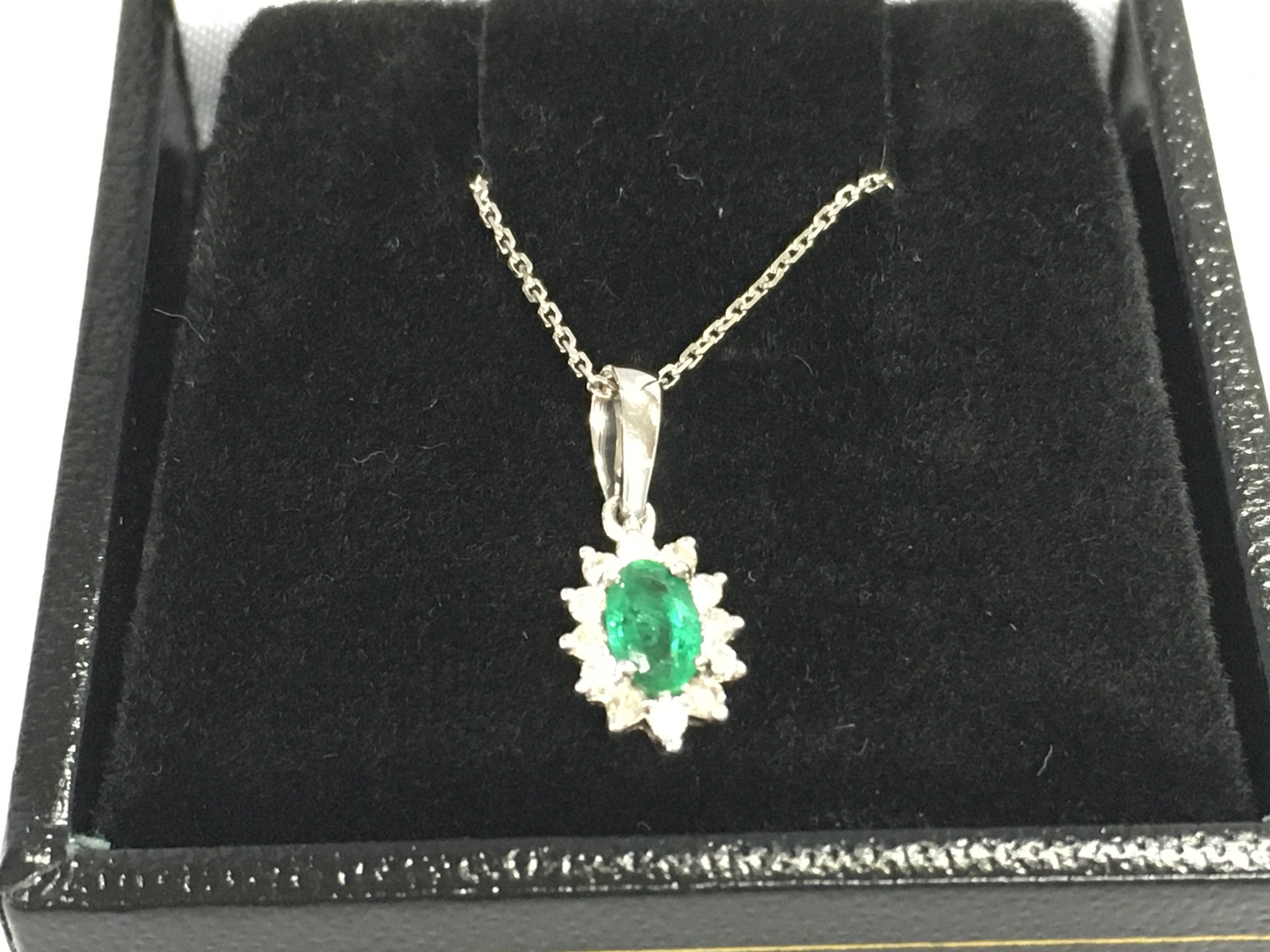 9ct white gold oval emerald and diamond cluster pendant on a 9ct white gold chain. Emerald 0.22ct and diamond 0.12ct.