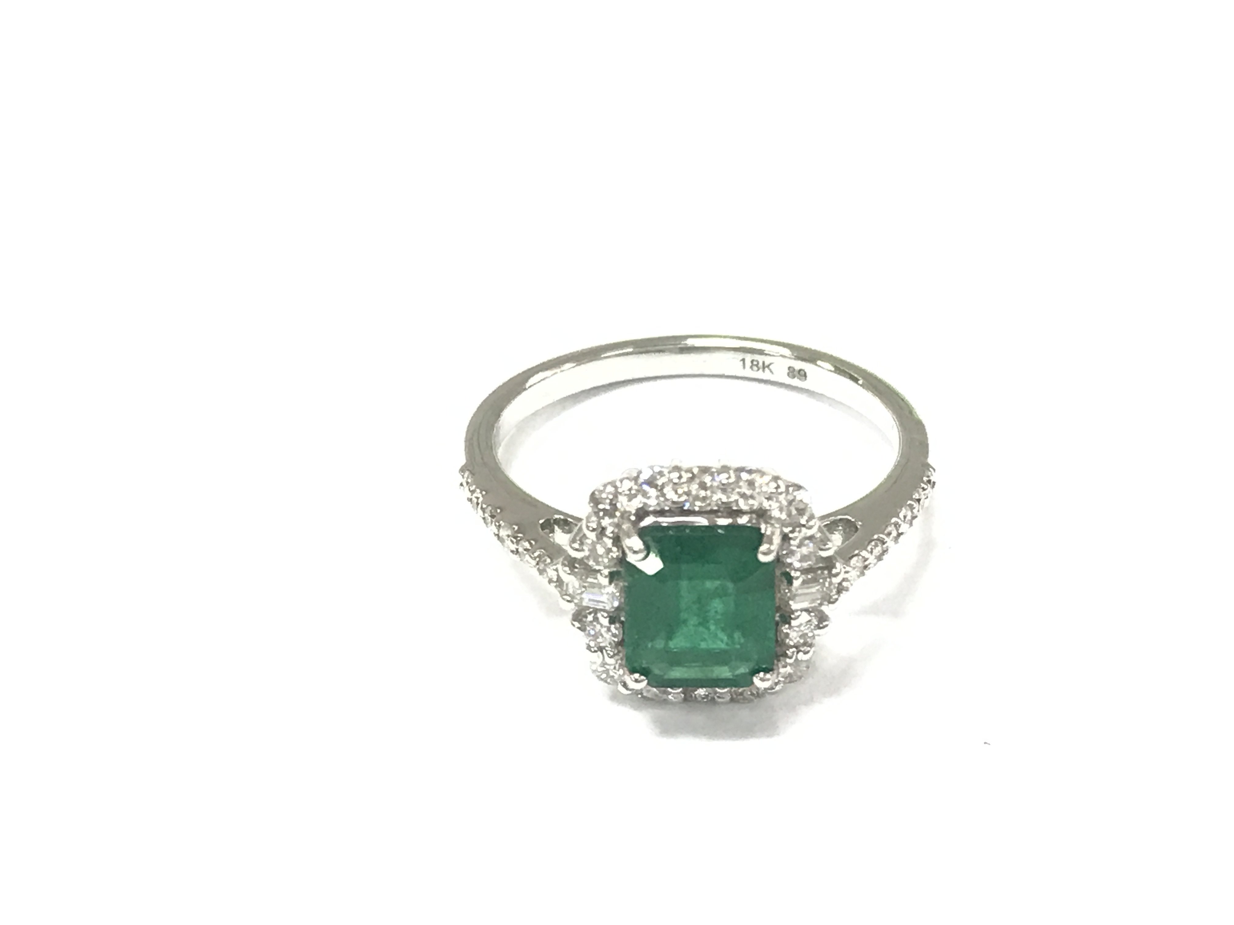 An 18ct white gold step cut emerald ring with round and baguette cut diamond border with further diamonds to the shoulders. Emeralds 1.13ct and diamonds 0.47ct approximately. Size N