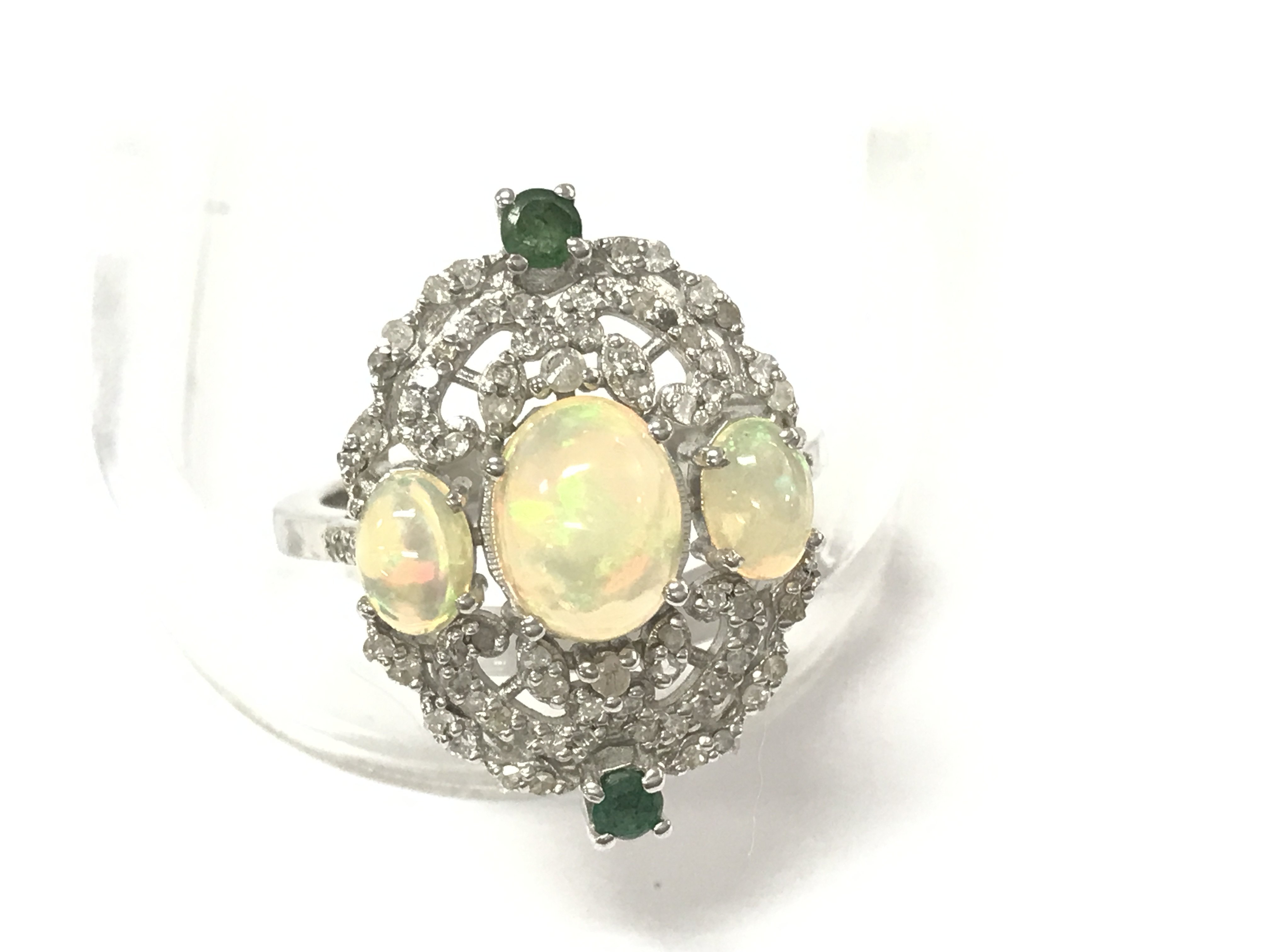 An ornate silver ring set with 3 oval cabochon opals 2 emeralds and several diamonds. Opals approx 2ct emeralds 0.20ct and diamonds 0.18ct. Size P 1/2