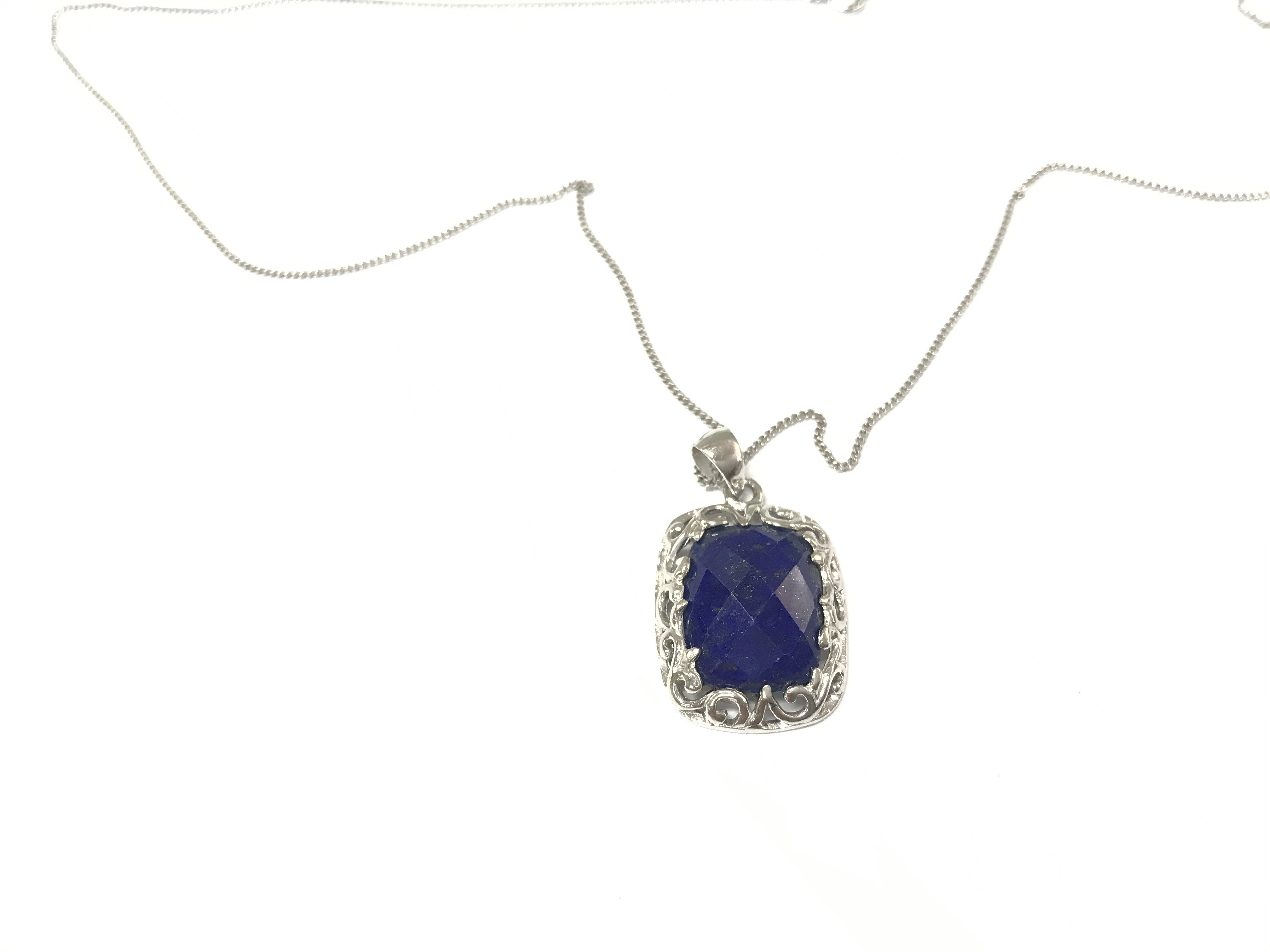 A silver pendant set with a cushion cut checkerboard lapis lazuli gemstone in an ornate mount on silver chain. Postage B