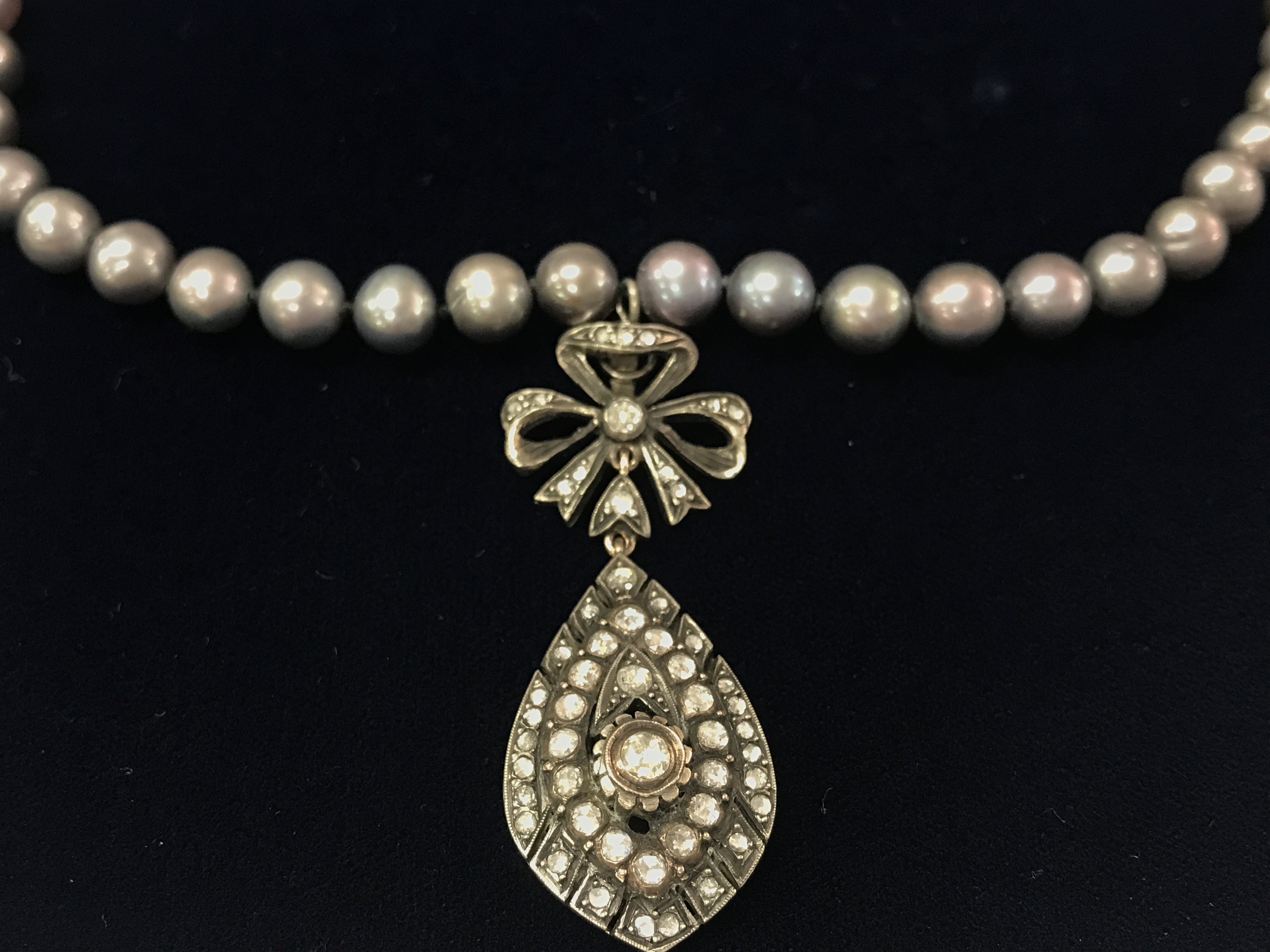 An unusual necklace strung with grey cultured Pearl with a white metal flamingo clasp and a silver and low carat gold hand made vintage style bow and pear shaped pendant set with rose cut diamonds approx 1ct. Postage B