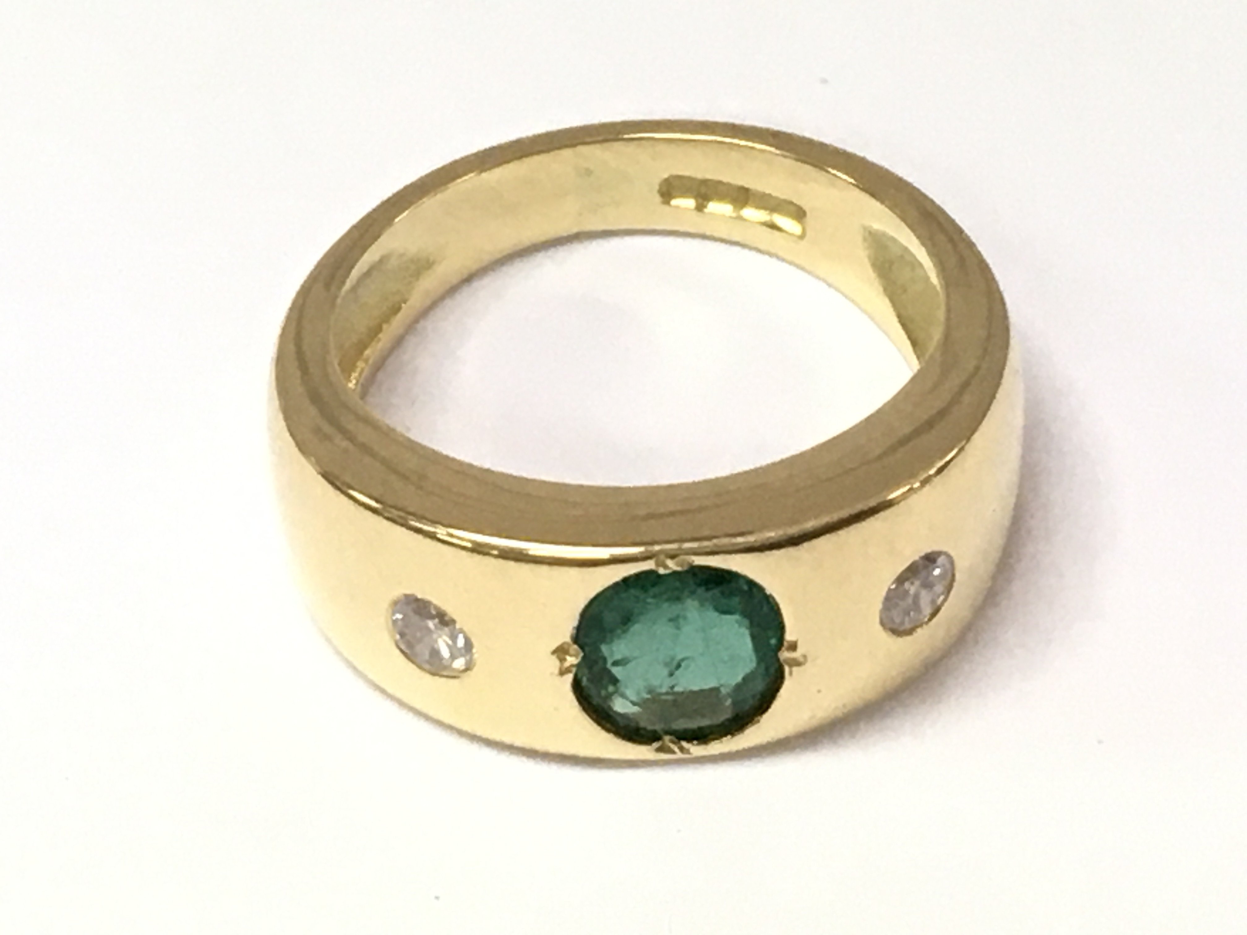 A gold ring inset with a central emerald flanked by diamonds. 6.13g and size F 1/2 approximately. Postage B