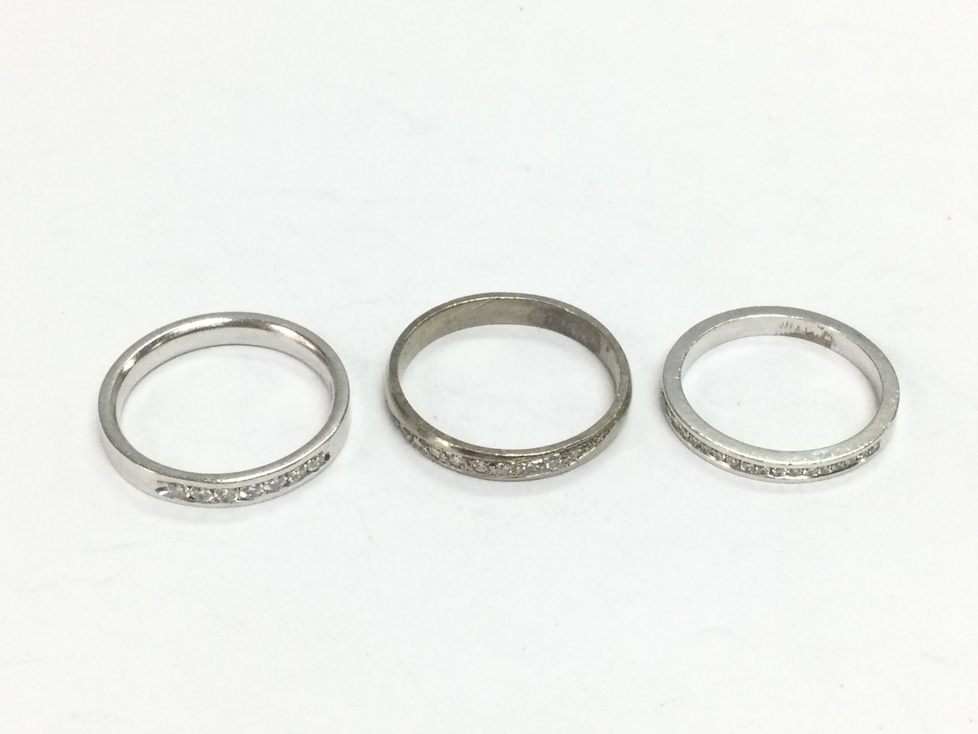 Three unmarked white gold half hoop diamond rings, approx sizes N, O and L. Total approx 9.7g. Shipping category A.