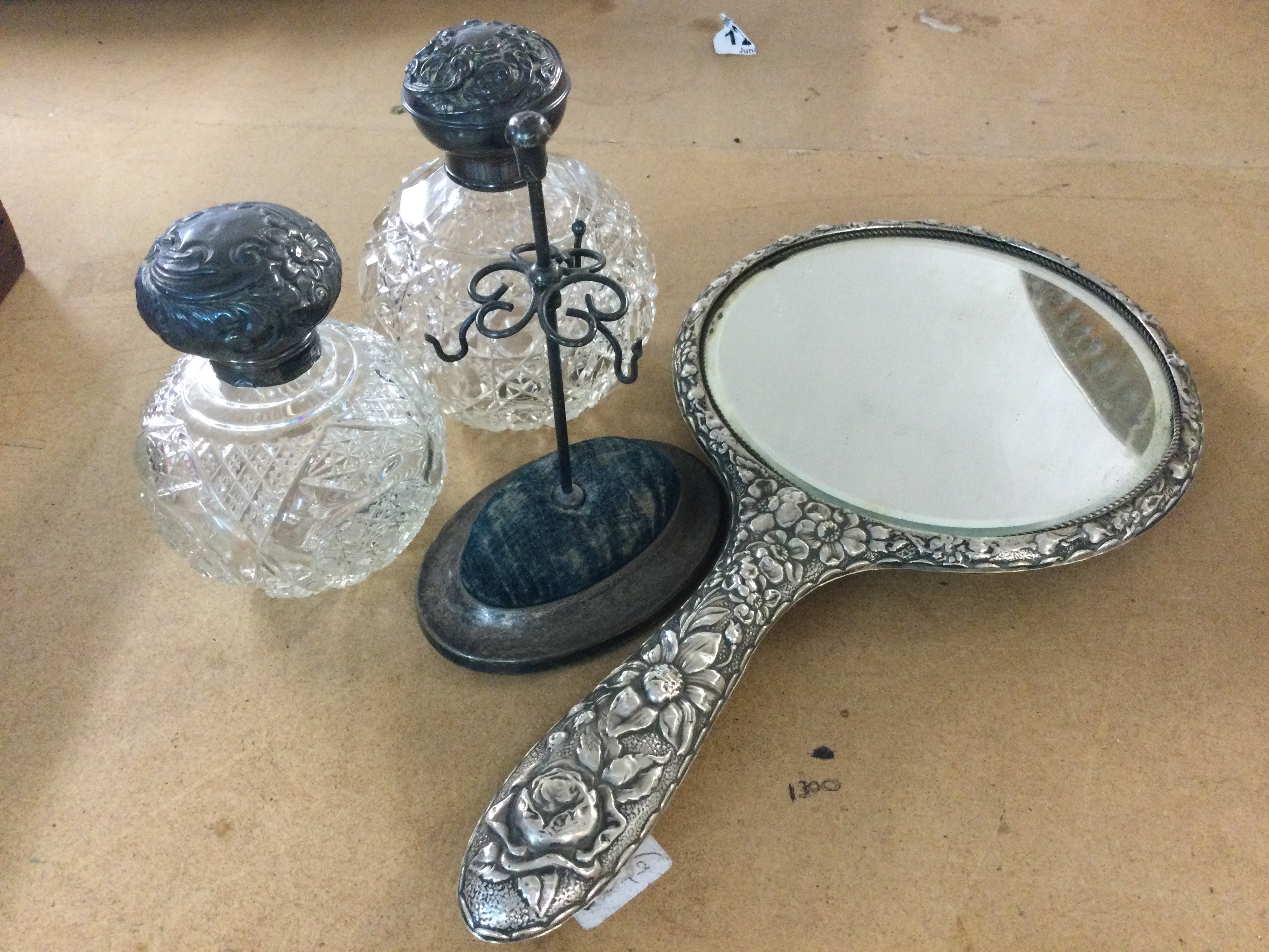 A silver hand mirror, two silver topped glass perfume bottles and a hat pin stand