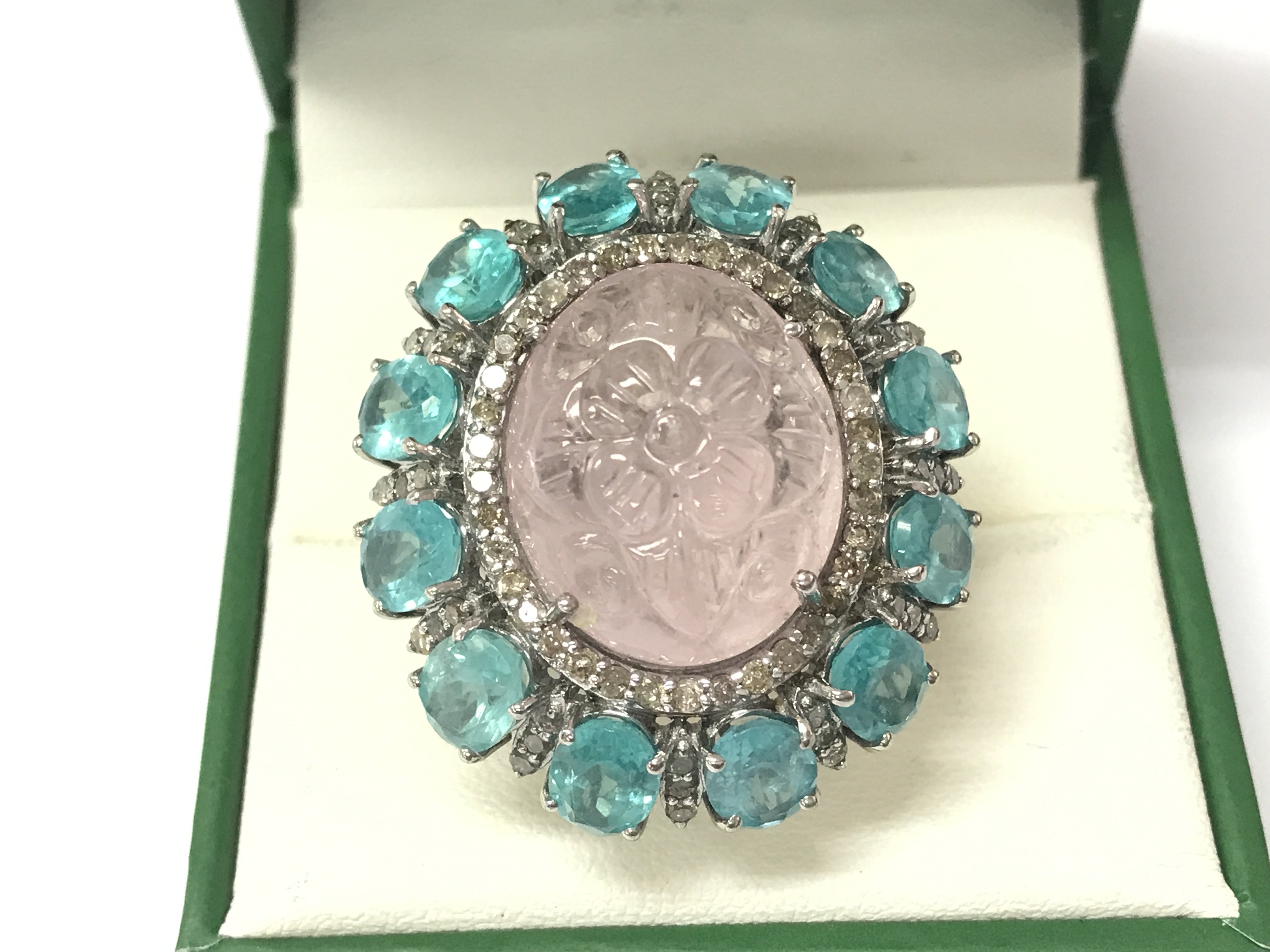 A large dress ring in white metal set with an oval carved morganite surrounded by oval apatites and diamonds. Morganite 19.18ct and apatities 10.26ct and 1.18ct diamonds approx. Size N
