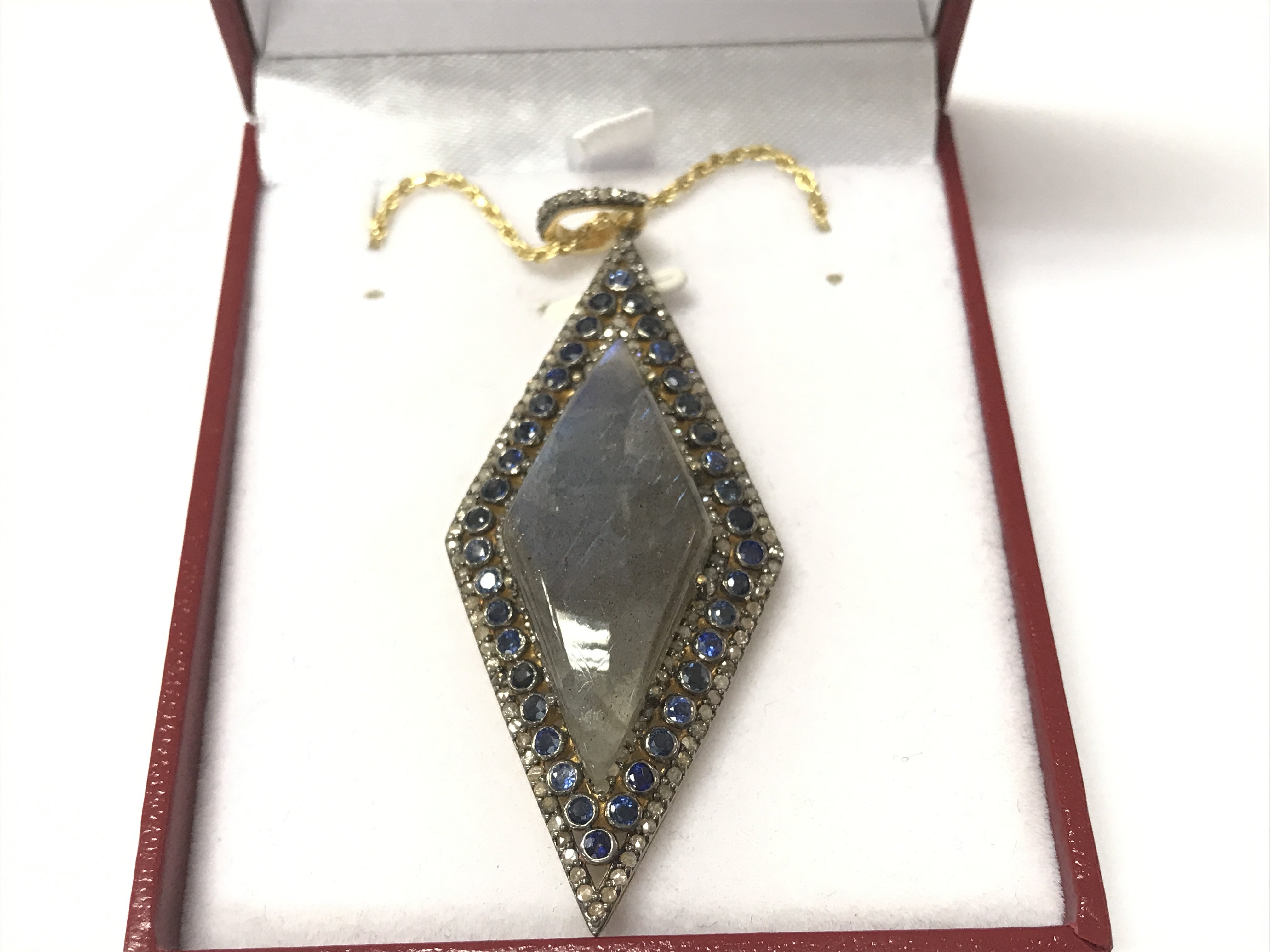 A large rhomboid pendant in yellow metal set with an oval cabochon labradorite surrounded by sapphires and diamonds on a gold plated silver chain. Labradorite 17.33ct sapphires 2.50ct and diamonds 1.25ct approximately.