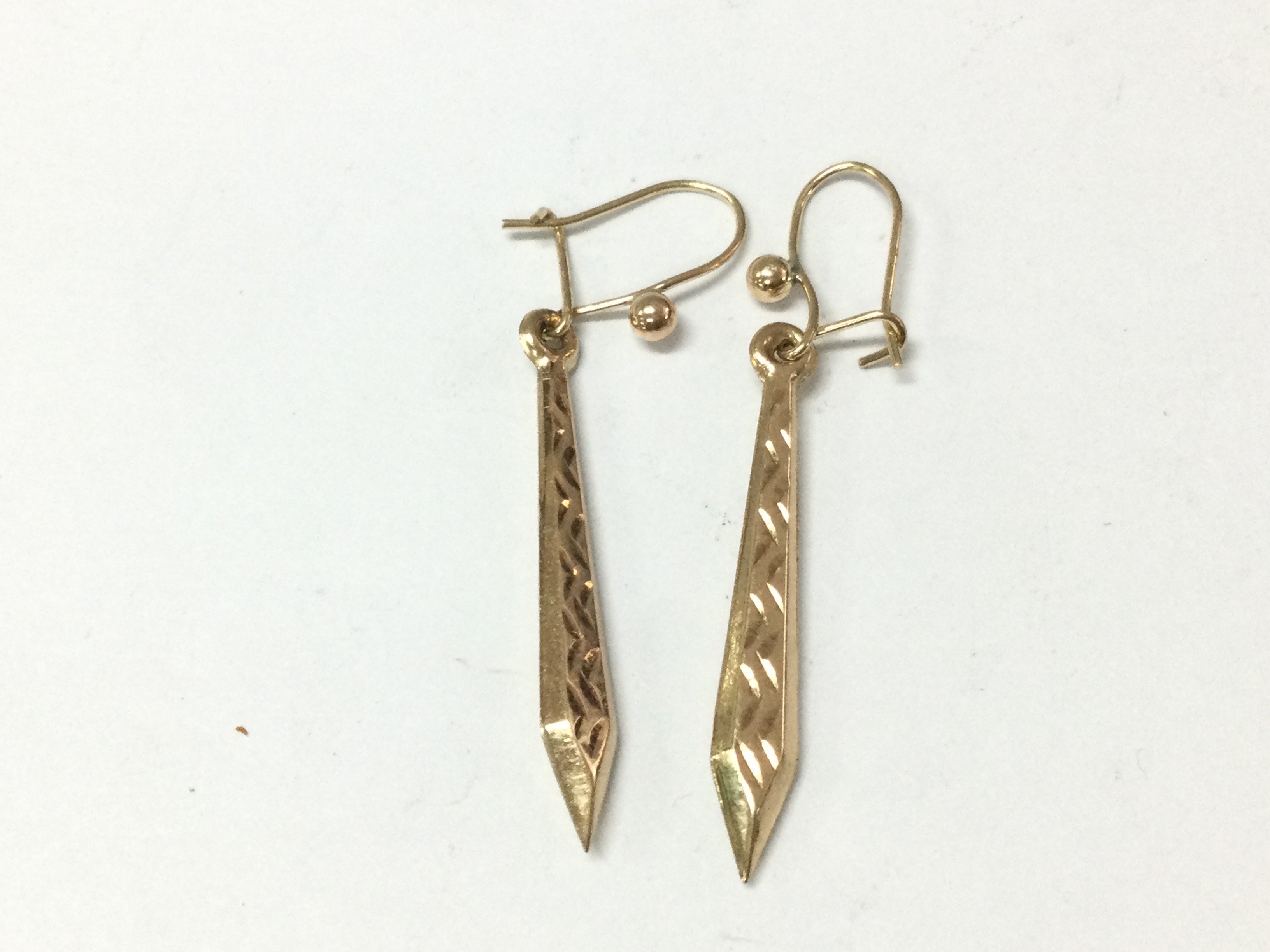 A pair of gold tone drop earrings.